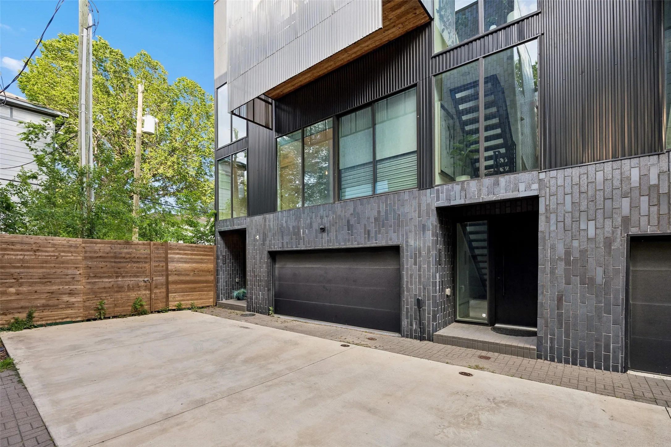 The property features a contemporary exterior with dark brickwork and large windows, complemented by a concrete driveway and an integrated garage