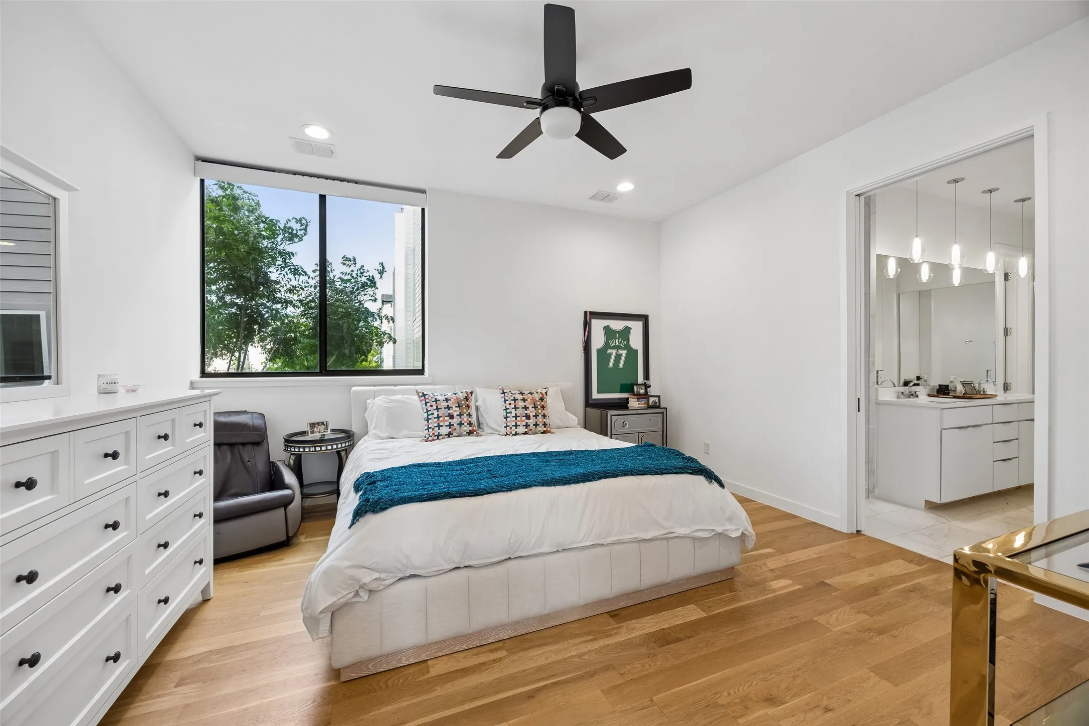 This room features light hardwood flooring, a ceiling fan, and a large window providing natural light