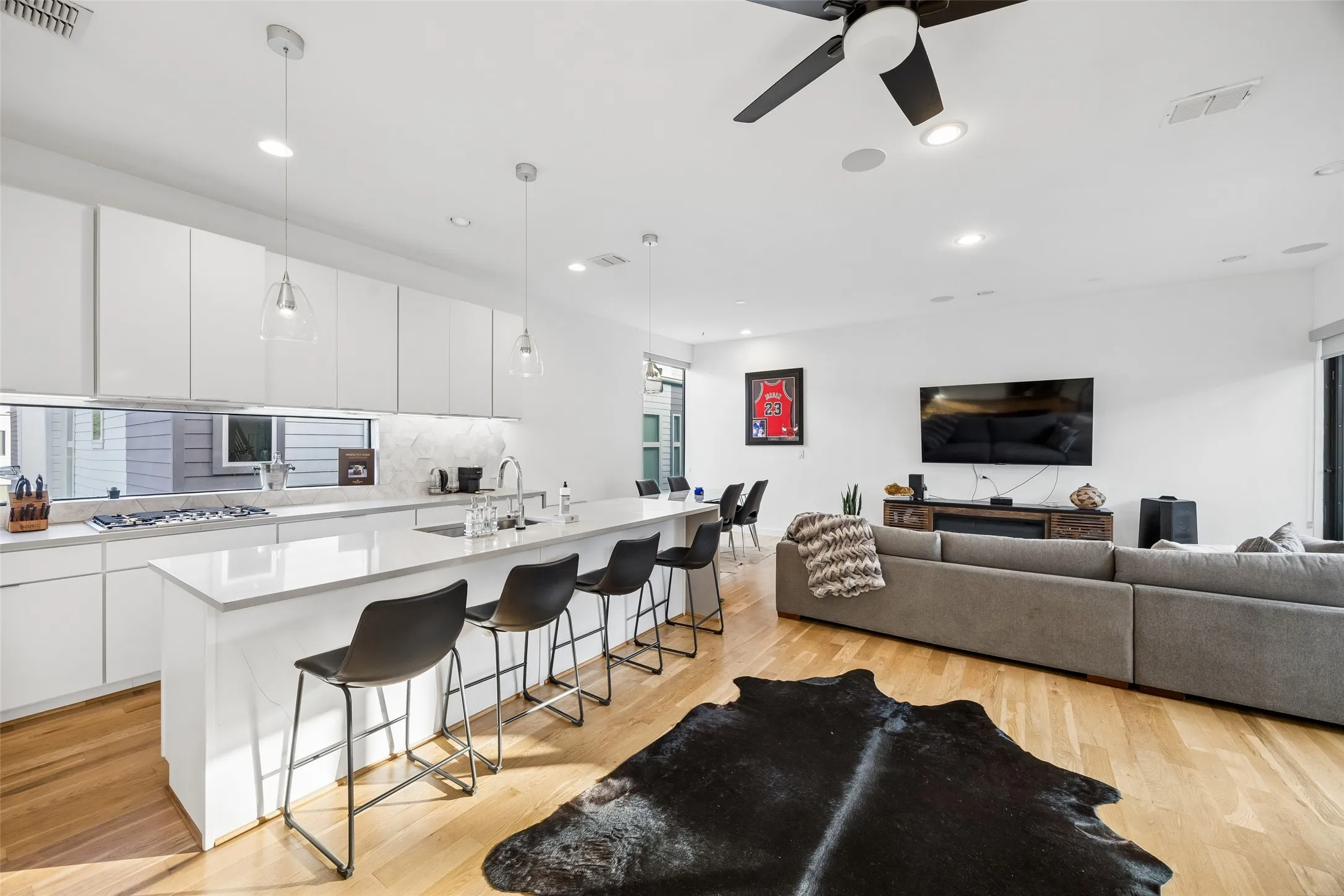 Open concept living area featuring hardwood flooring, a modern kitchen with a large island, white cabinetry, and stainless steel appliances