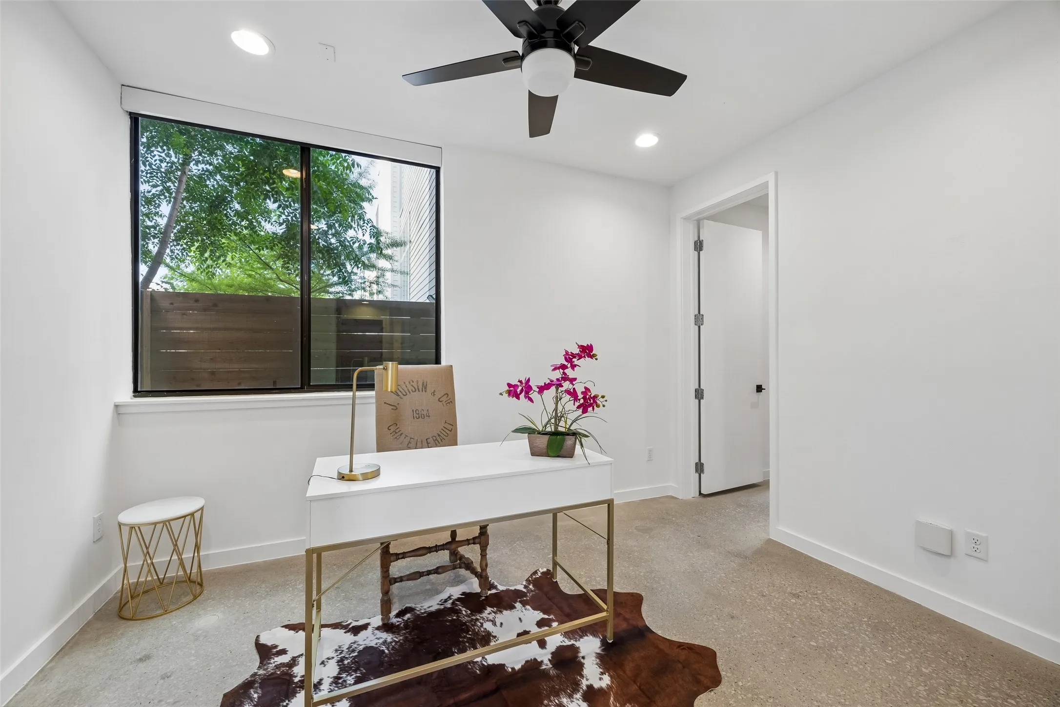This room features a large window with views of greenery and a wooden fence, recessed lighting, and a ceiling fan