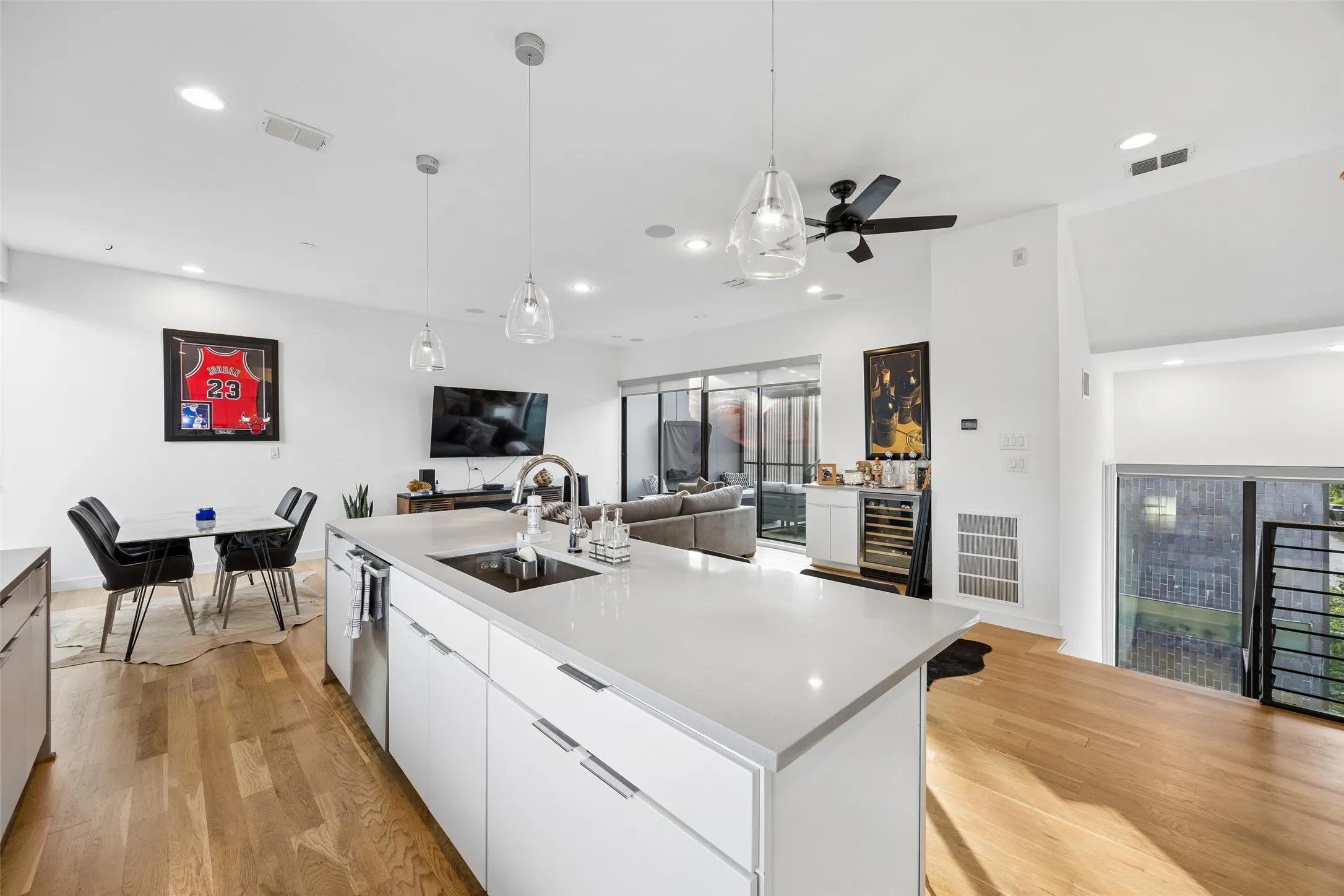 Open concept living area with light hardwood floors, a kitchen island featuring a sink and white cabinetry, and recessed lighting