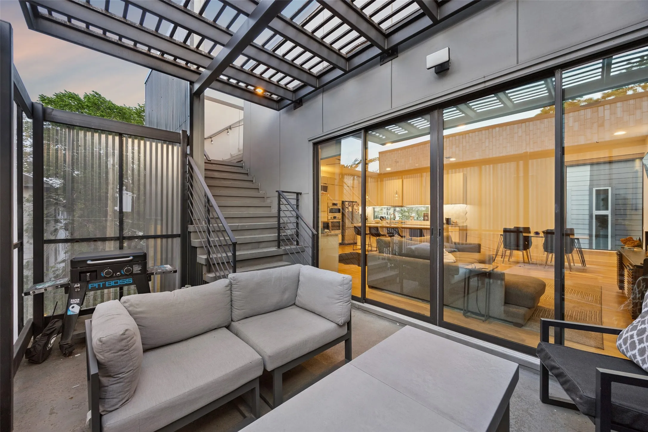 Private outdoor patio area with a pergola, a metal staircase, and sliding glass doors that open to the interior