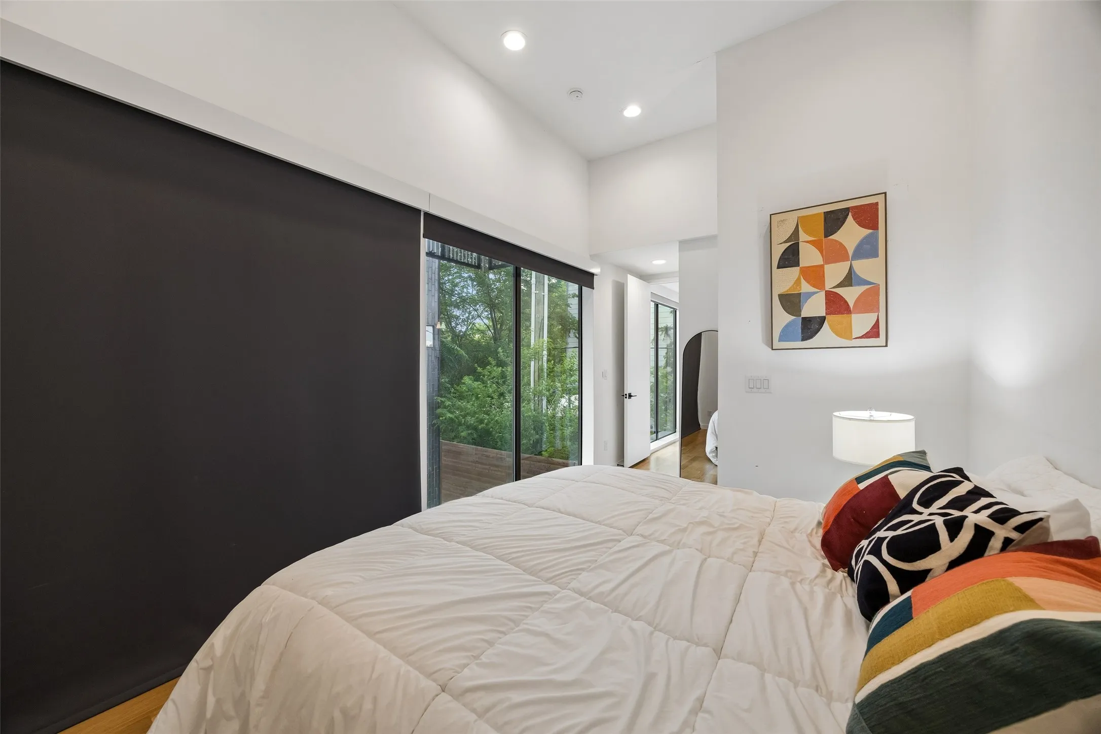 This room features high vaulted ceilings with recessed lighting, and a full-height glass door providing views of the surrounding greenery