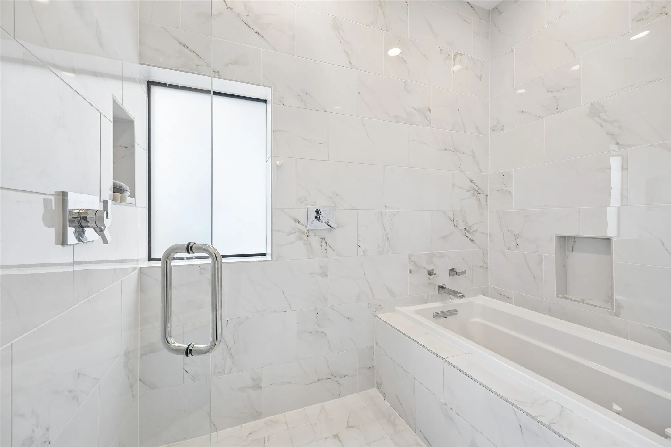 Modern bathroom featuring large format white marble-style tiles, a built-in bathtub, a walk-in shower with a glass enclosure, and contemporary chrome fixtures