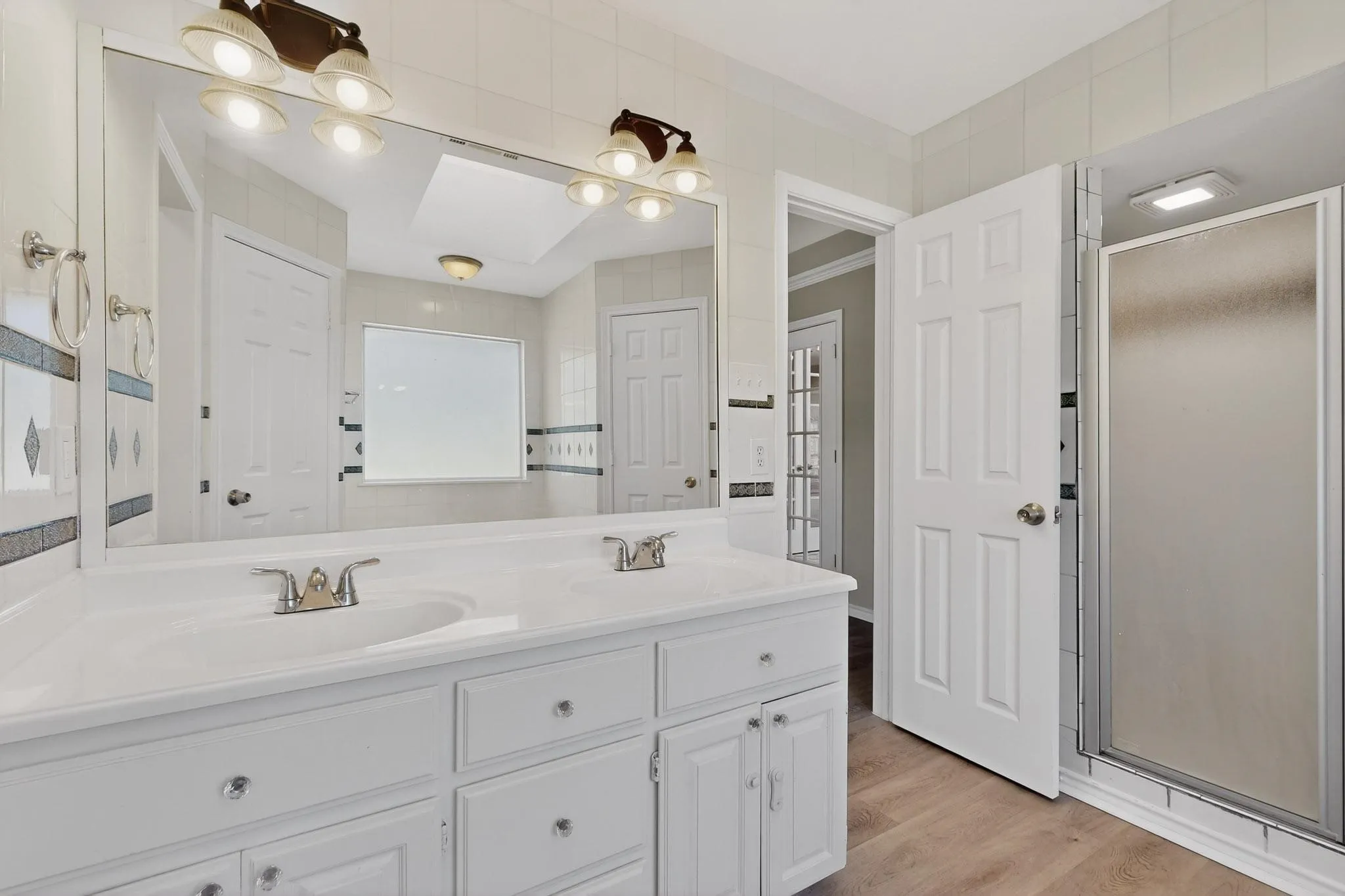Bathroom with double vanity, light wood finished floors, and a stall shower
