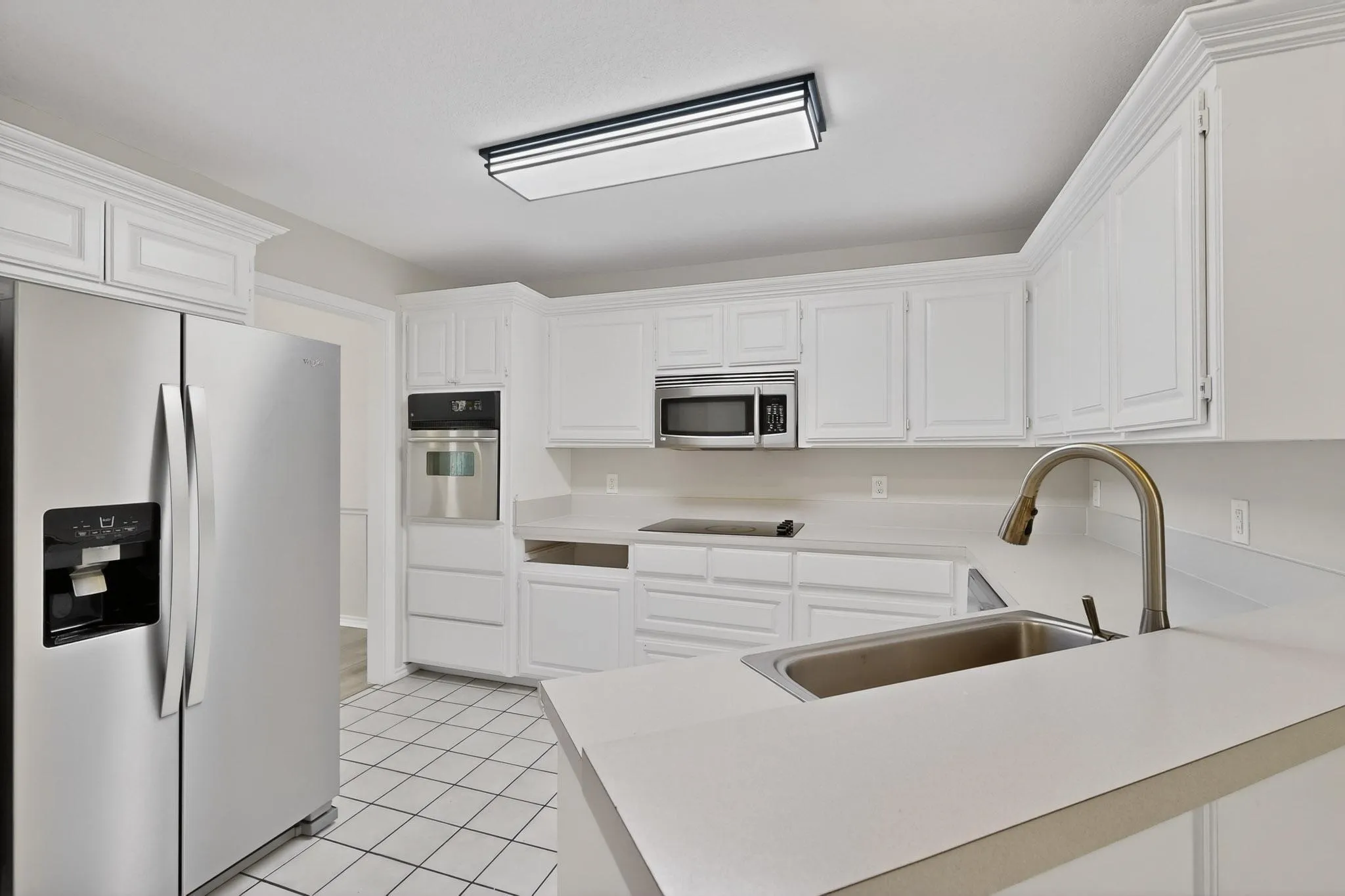 Kitchen with stainless steel appliances, light countertops, white cabinetry, and light tile patterned flooring