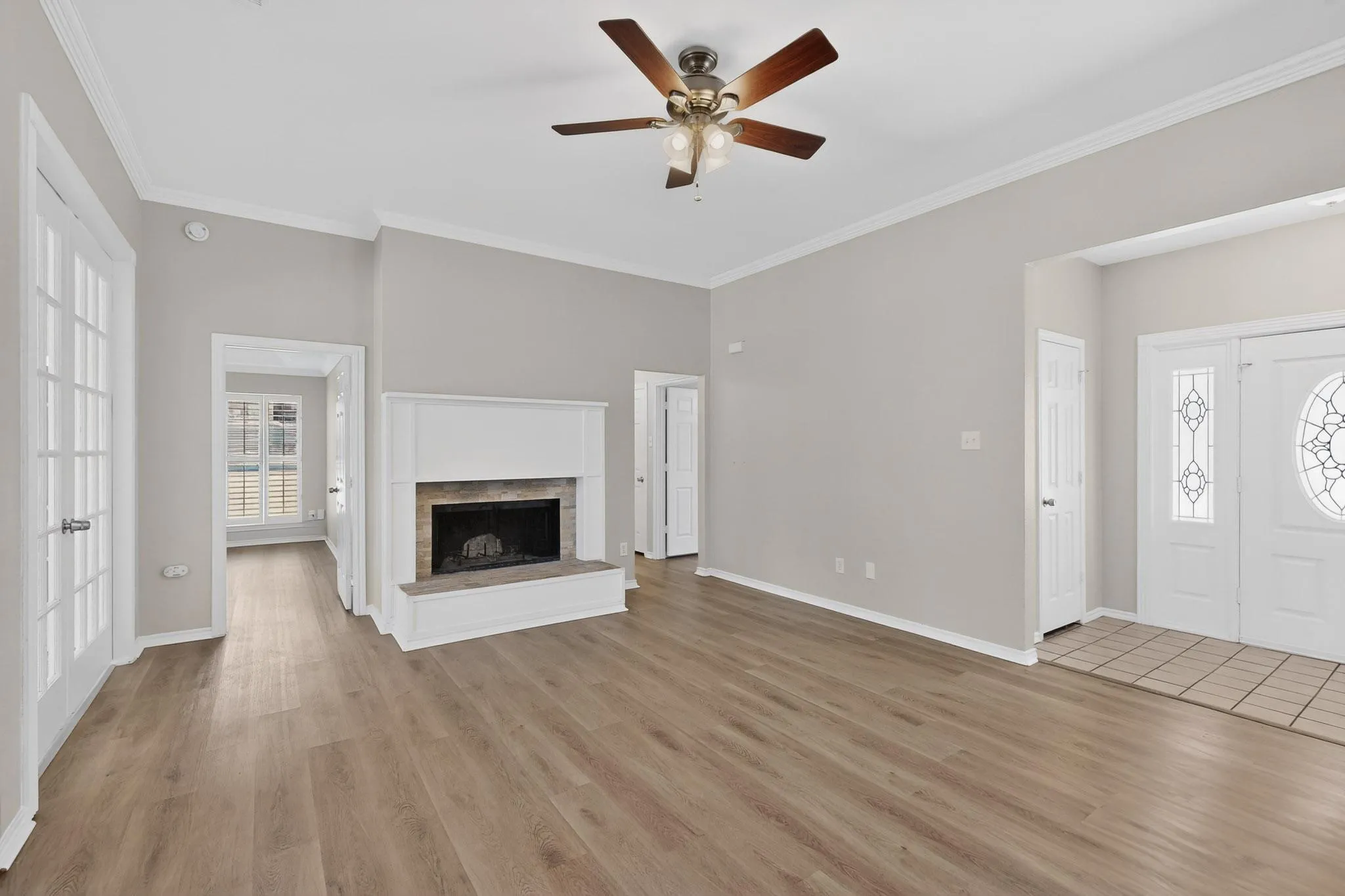 Unfurnished living room with a brick fireplace, a ceiling fan, light wood-type flooring, and crown molding