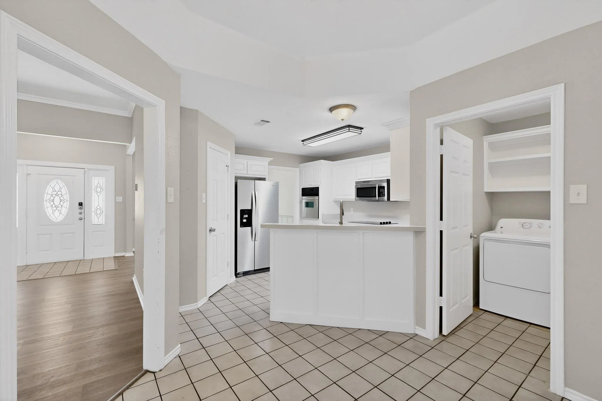 Kitchen with washer / dryer, light countertops, white cabinets, stainless steel appliances, and light tile patterned floors
