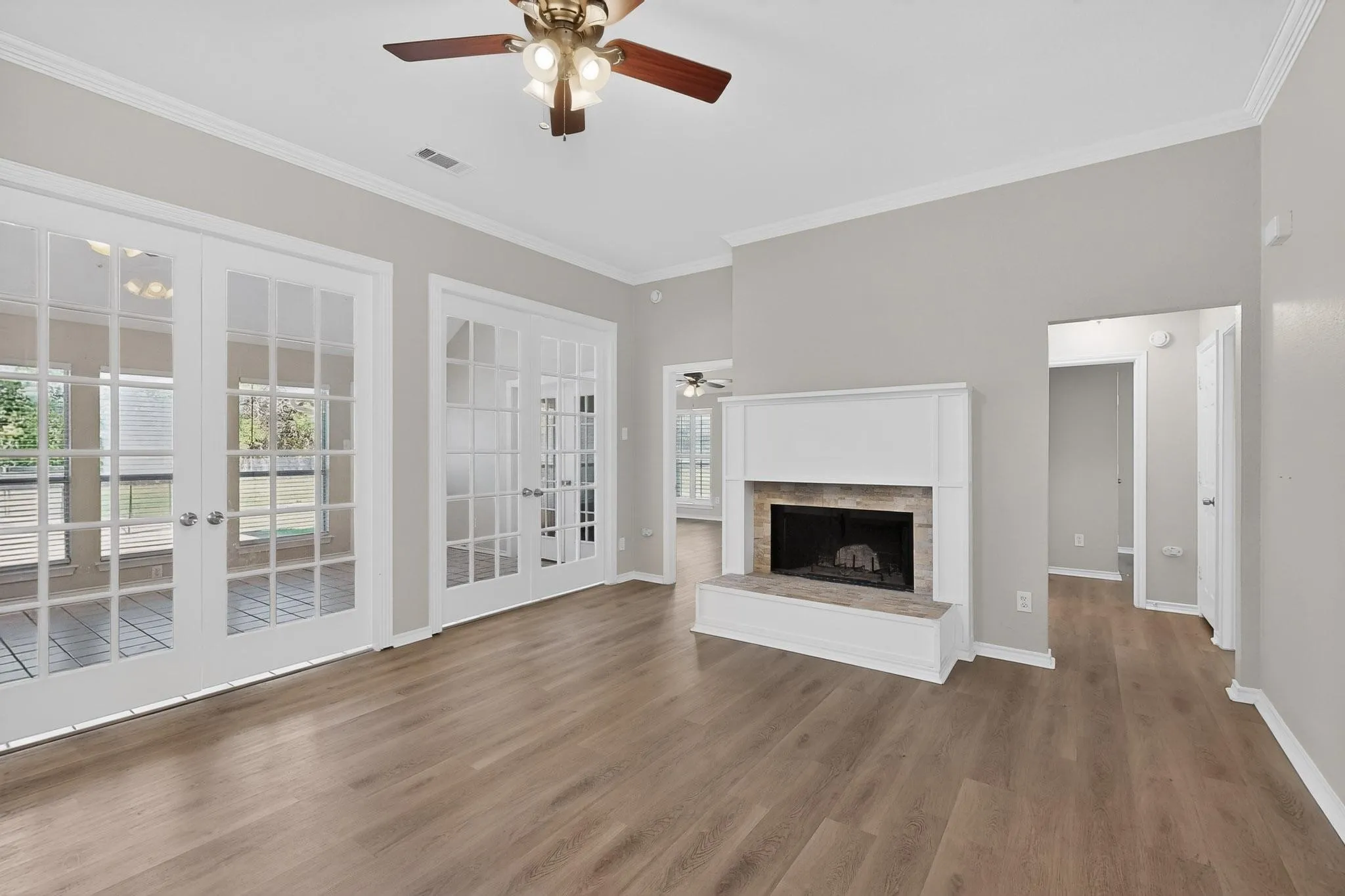 Unfurnished living room with ceiling fan, french doors, ornamental molding, a fireplace with raised hearth, and dark wood finished floors