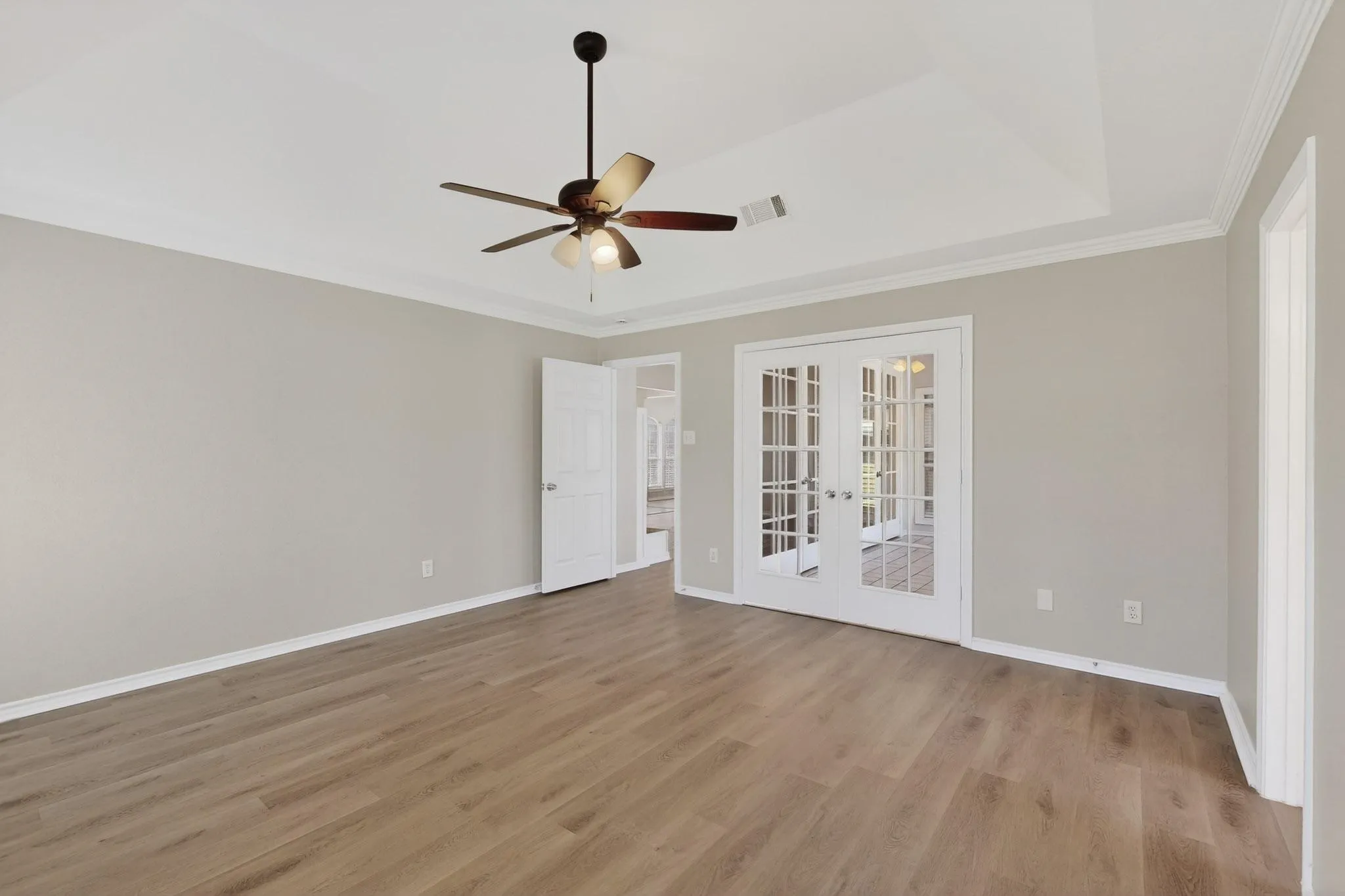 Empty room with french doors, a ceiling fan, light wood-style floors, and ornamental molding