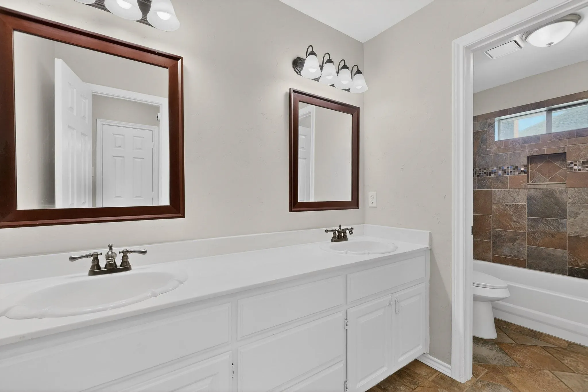Full bath featuring double vanity, light stone finish floors, and bathing tub / shower combination