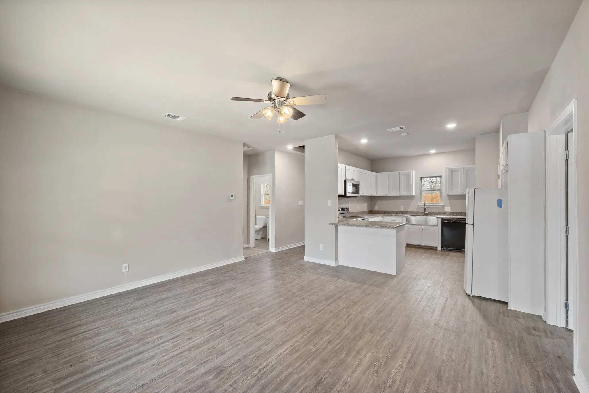 Kitchen with open floor plan, black appliances, ceiling fan, light wood-style floors, and white cabinetry
