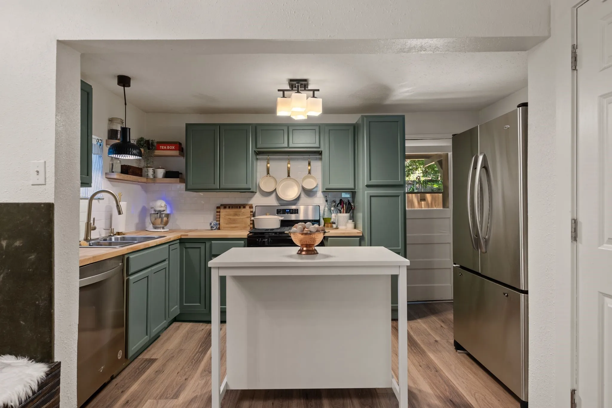 Kitchen with green cabinetry, appliances with stainless steel finishes, decorative backsplash, open shelves, and light wood-style flooring
