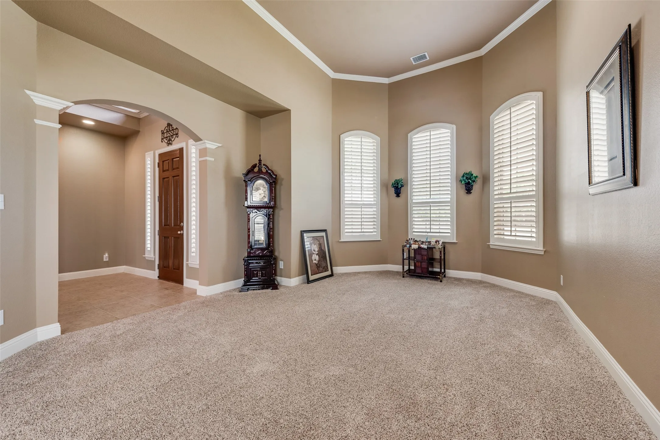 Empty room with arched walkways, light colored carpet, ornamental molding, and decorative columns