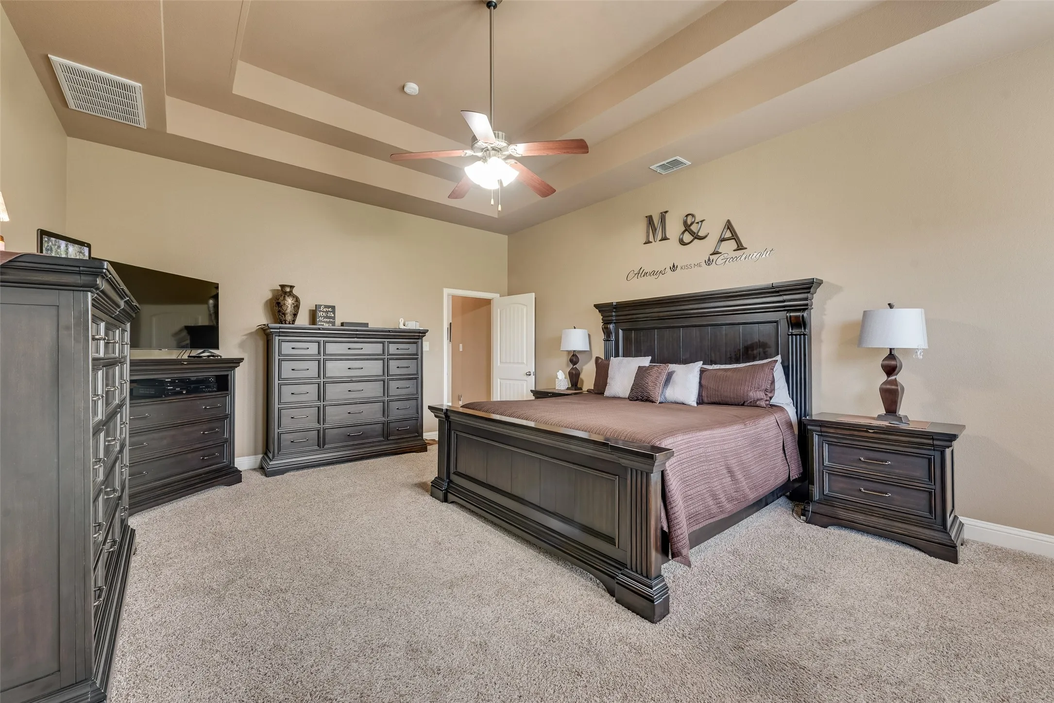 Bedroom with a tray ceiling, light colored carpet, and a ceiling fan