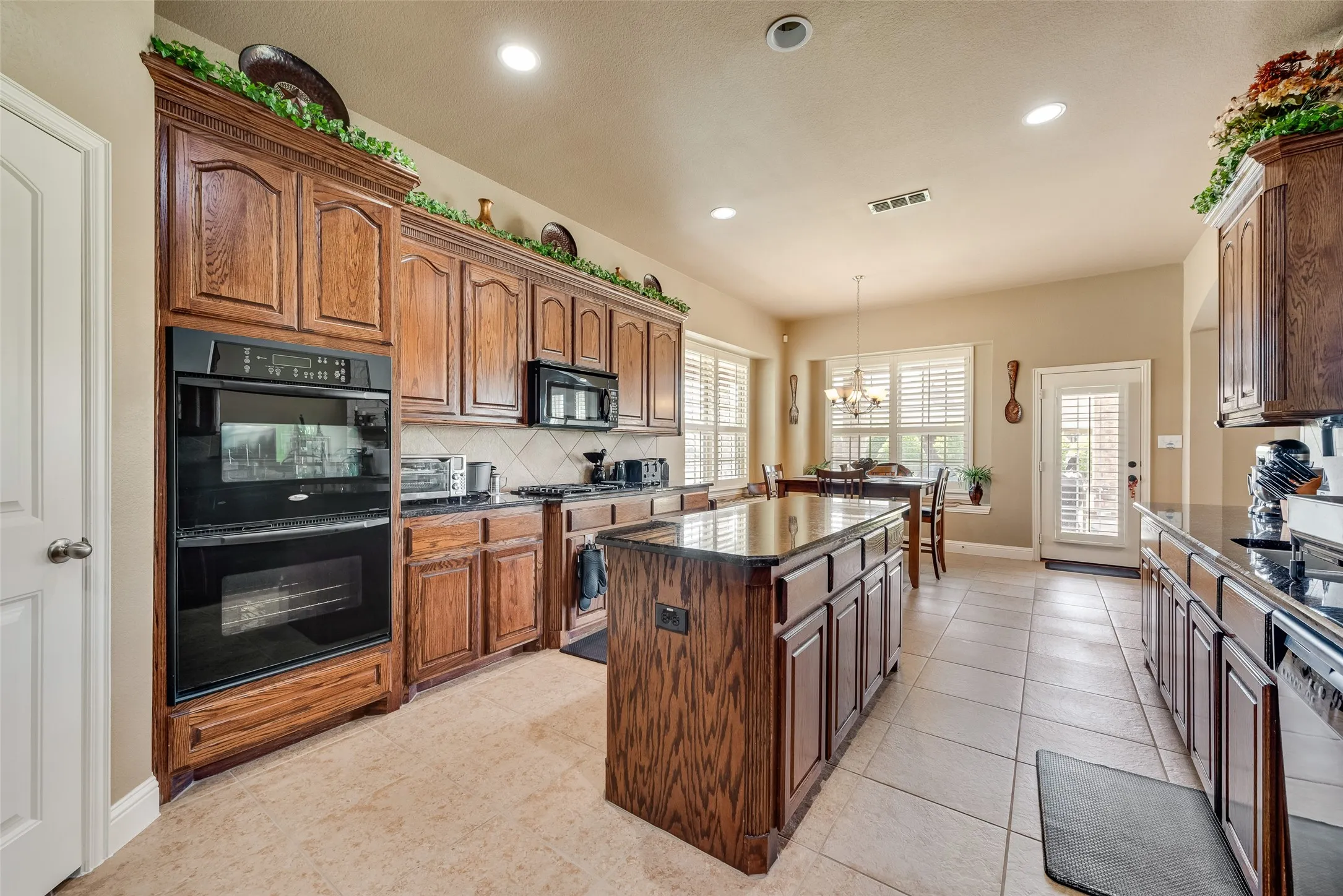 Kitchen featuring black appliances, a kitchen island, suspended lighting, light tile patterned floors, and wood finish cabinetry