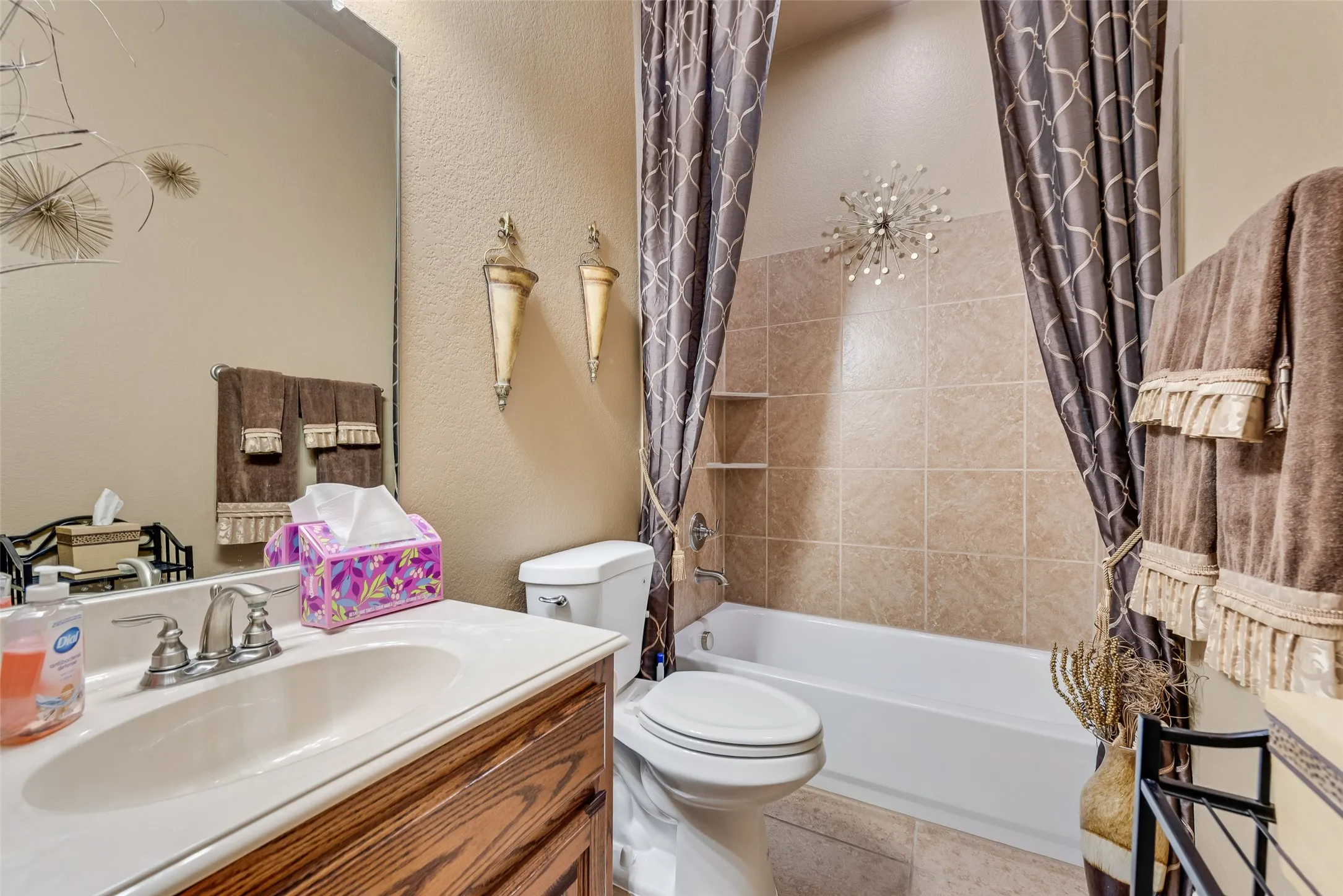 Bathroom featuring vanity, shower / bath combo with shower curtain, a textured wall, and light tile patterned floors