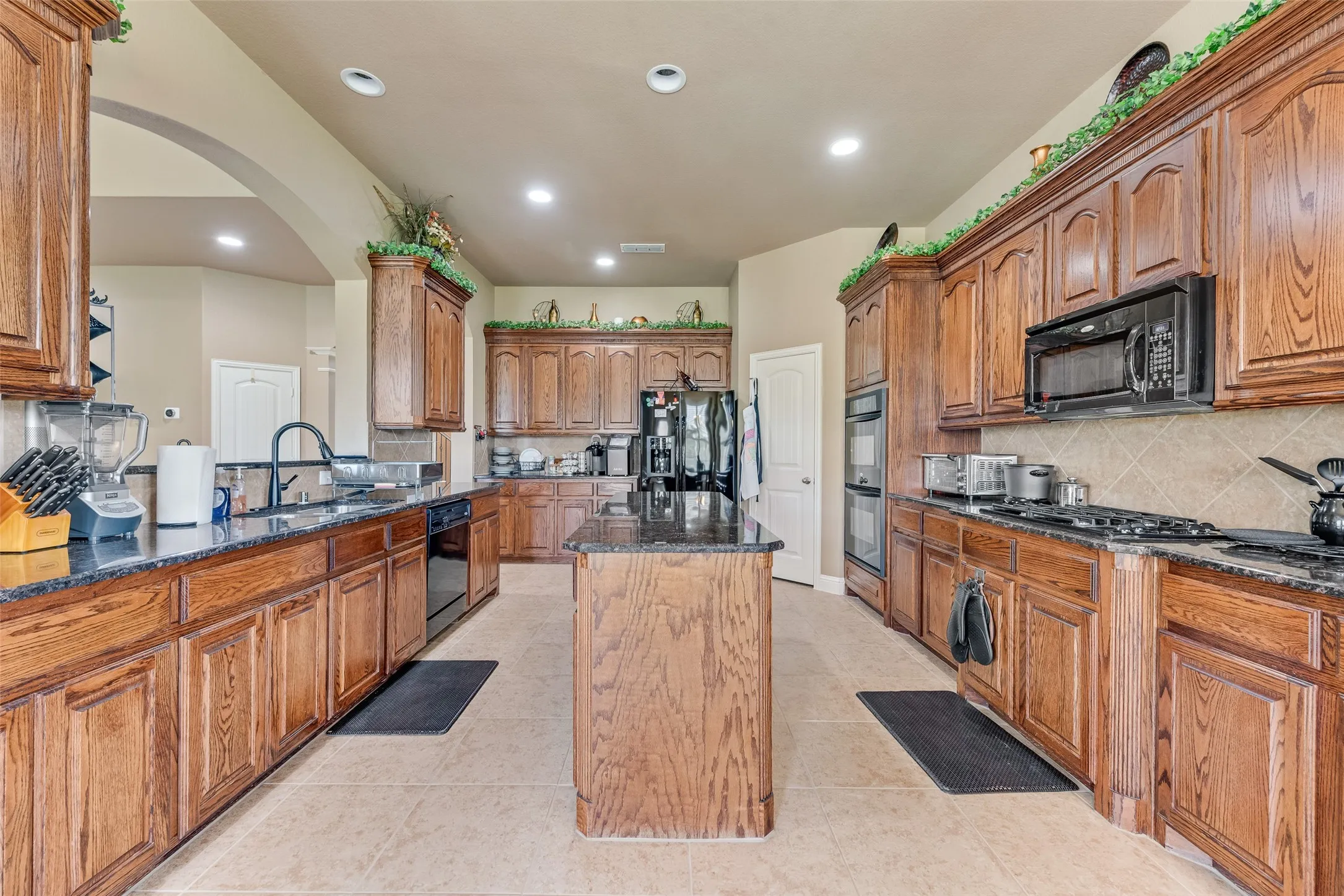Kitchen featuring wood finish cabinetry, dark stone counters, tasteful backsplash, a kitchen island, and recessed lighting