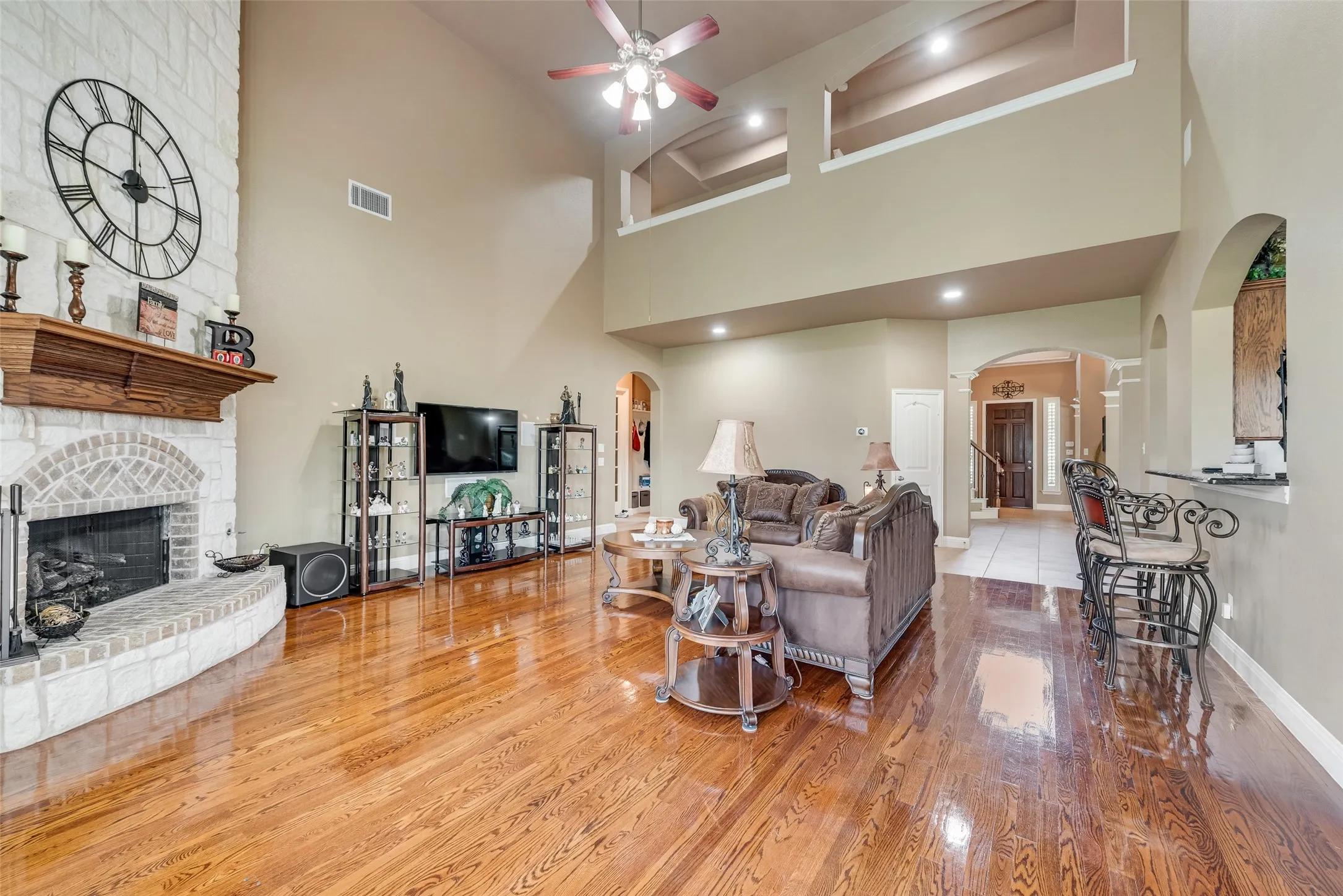 Living room with arched walkways, a fireplace, ceiling fan, light wood-style floors, and vaulted ceiling
