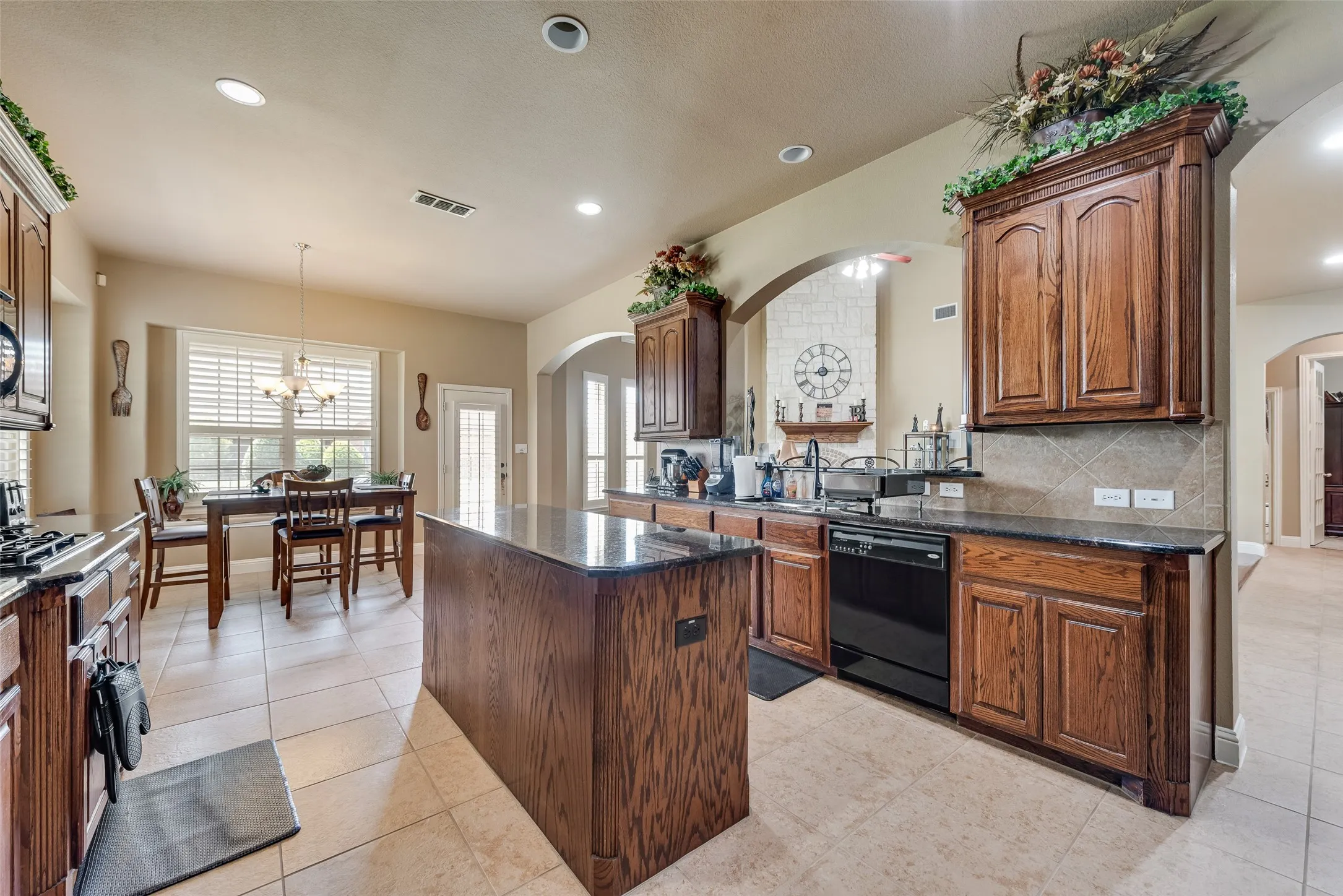 Kitchen featuring arched walkways, a kitchen island, dark stone countertops, black dishwasher, and hanging lights