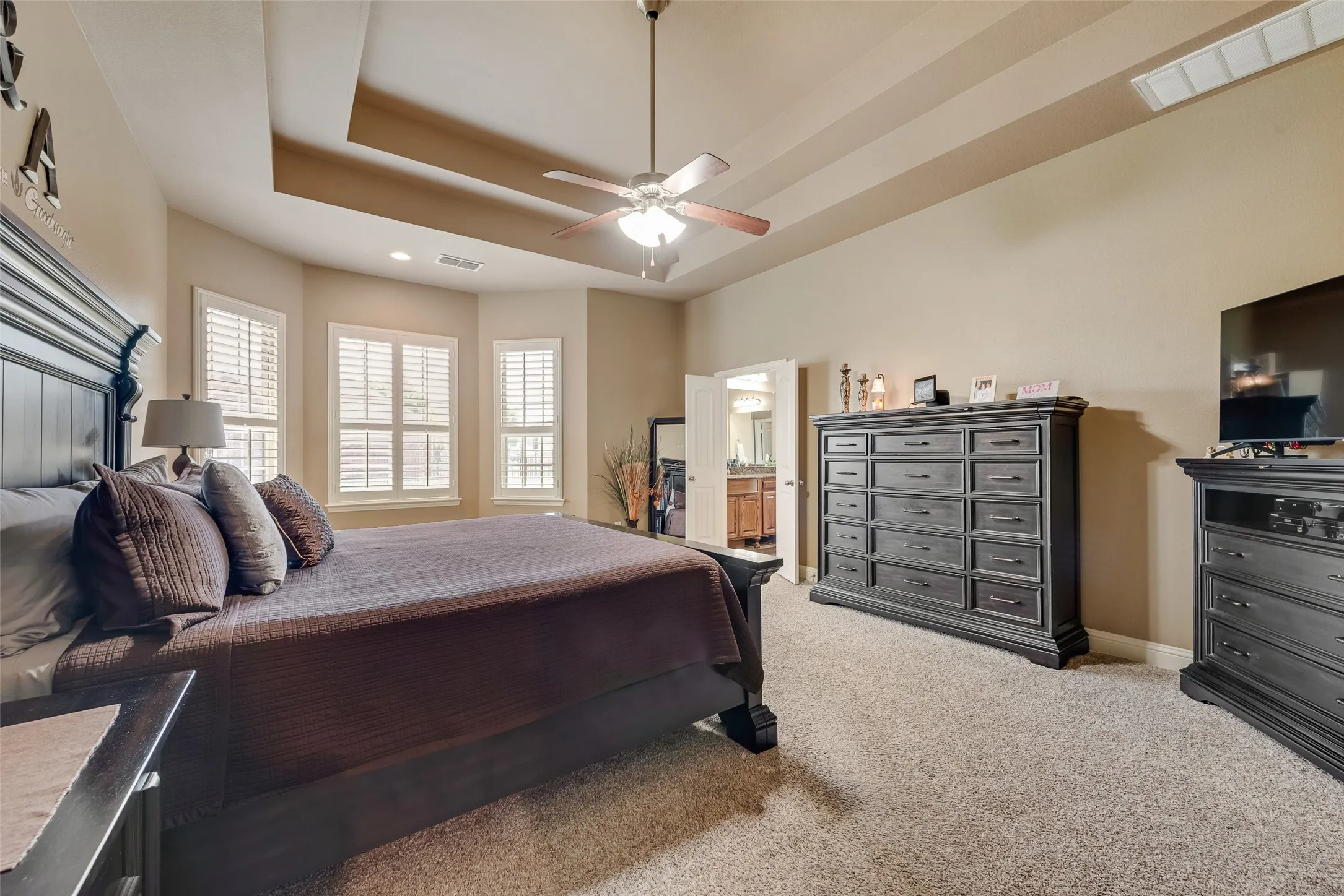 Bedroom featuring light carpet, ensuite bathroom, a ceiling fan, and a raised ceiling