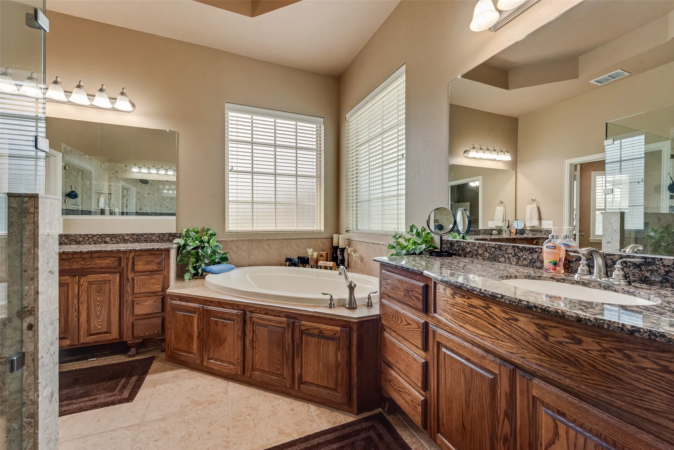 Bathroom featuring a bath, two vanities, a shower stall, and light tile patterned floors