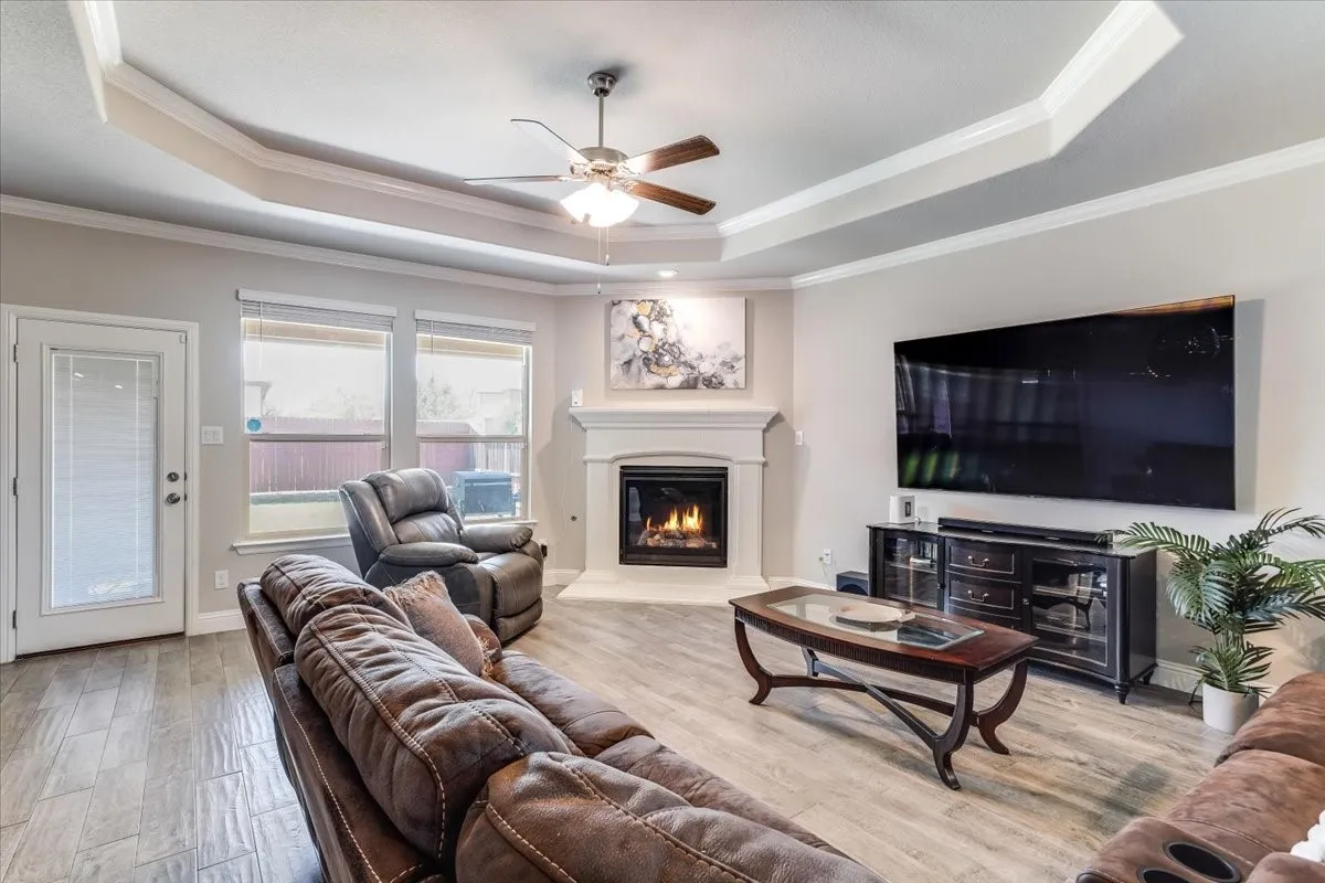 Tray ceiling with crown molding, ceiling fan, wood-finish flooring, fireplace with mantel, and recessed lighting