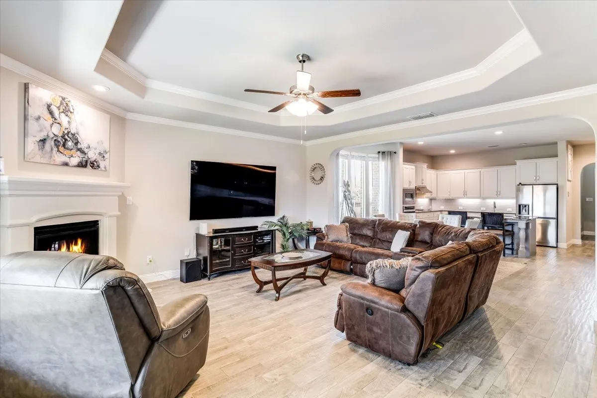 Tray ceiling with crown molding, recessed lighting, ceiling fan, wood-finish flooring, and a built-in fireplace