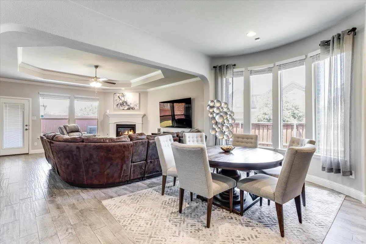 Tray ceiling with ceiling fan, fireplace with mantel, wood-finish flooring, and a curved wall of windows