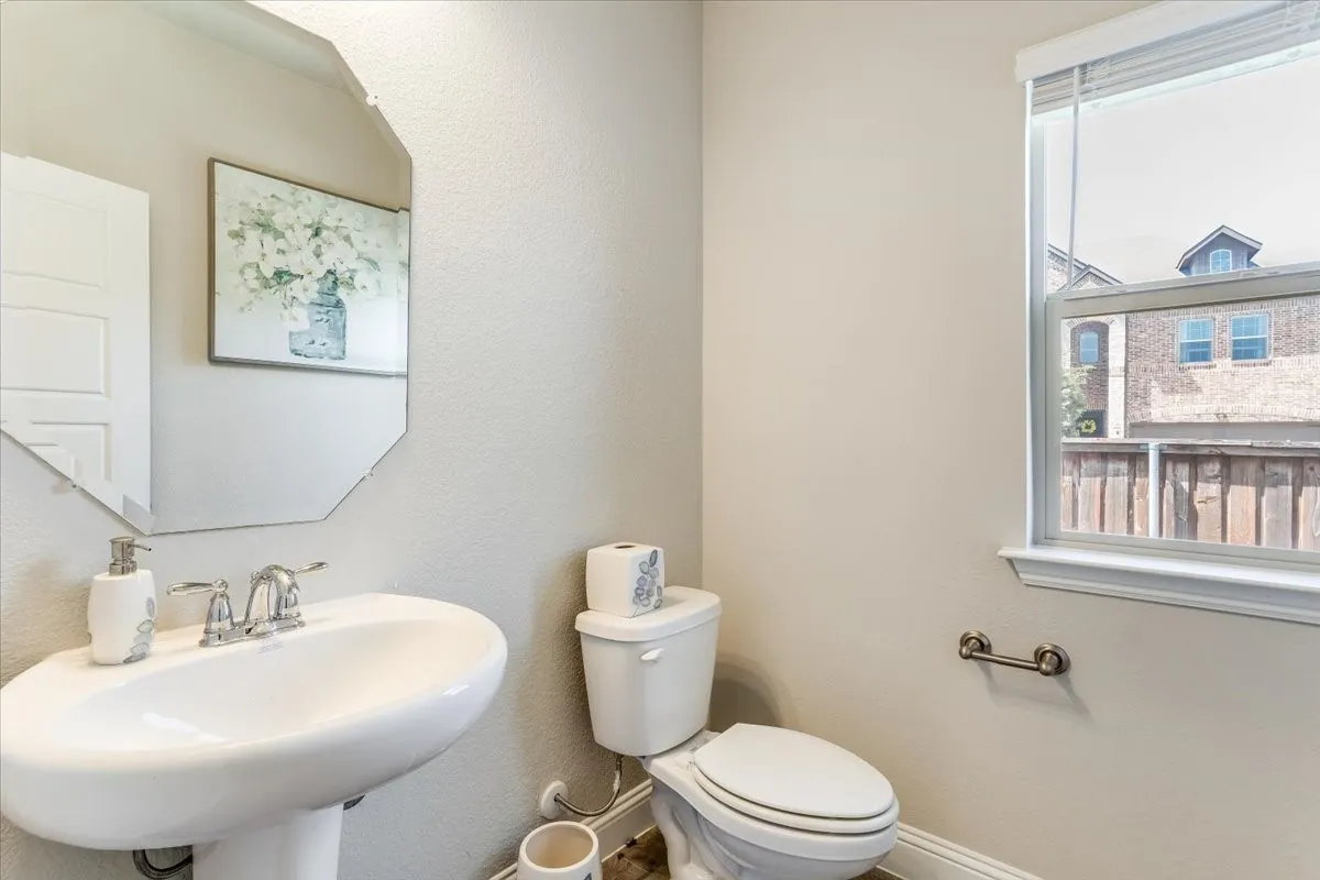 Pedestal sink with chrome faucet, octagonal wall mirror, white toilet, and a window with blinds