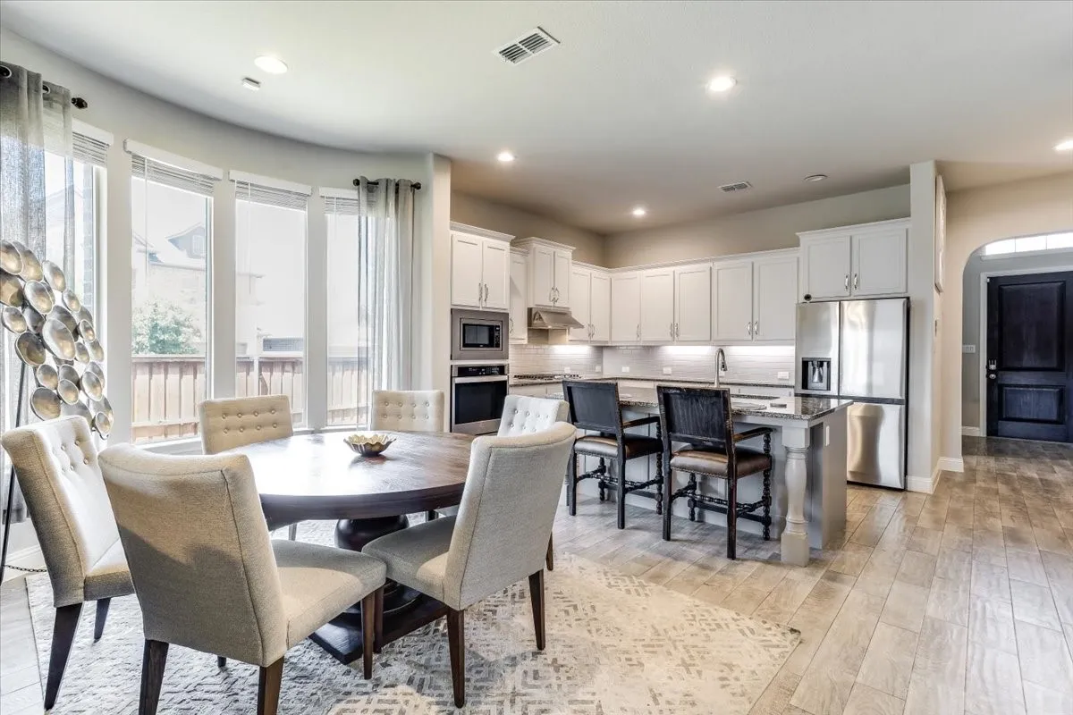 Open-concept kitchen and dining area featuring a curved bay window, light wood-finish flooring, white cabinetry, and stainless steel appliances
