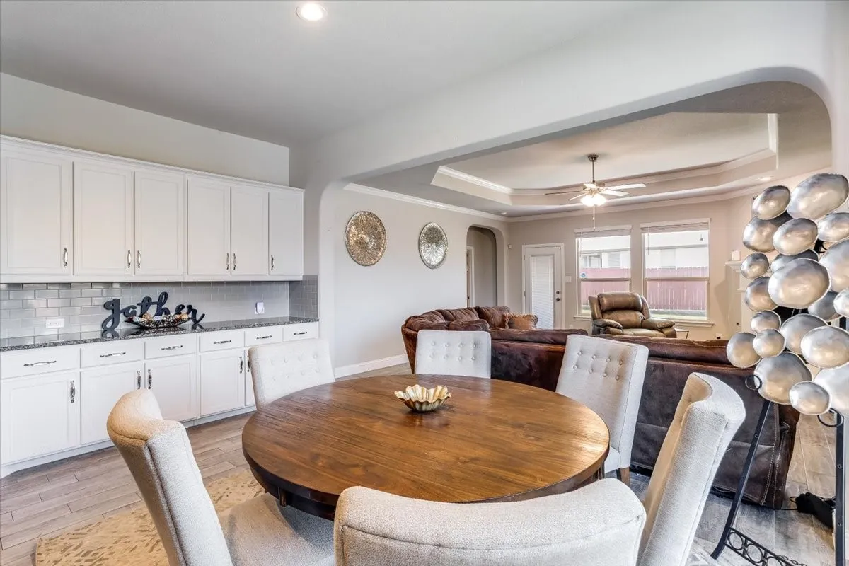 Built-in white cabinetry with granite countertops, subway tile backsplash, wood-finish flooring, and a tray ceiling
