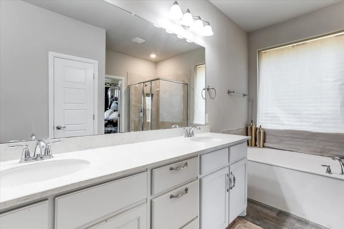 Dual undermount sinks with chrome fixtures, white cabinetry, integrated soaking tub, and enclosed shower