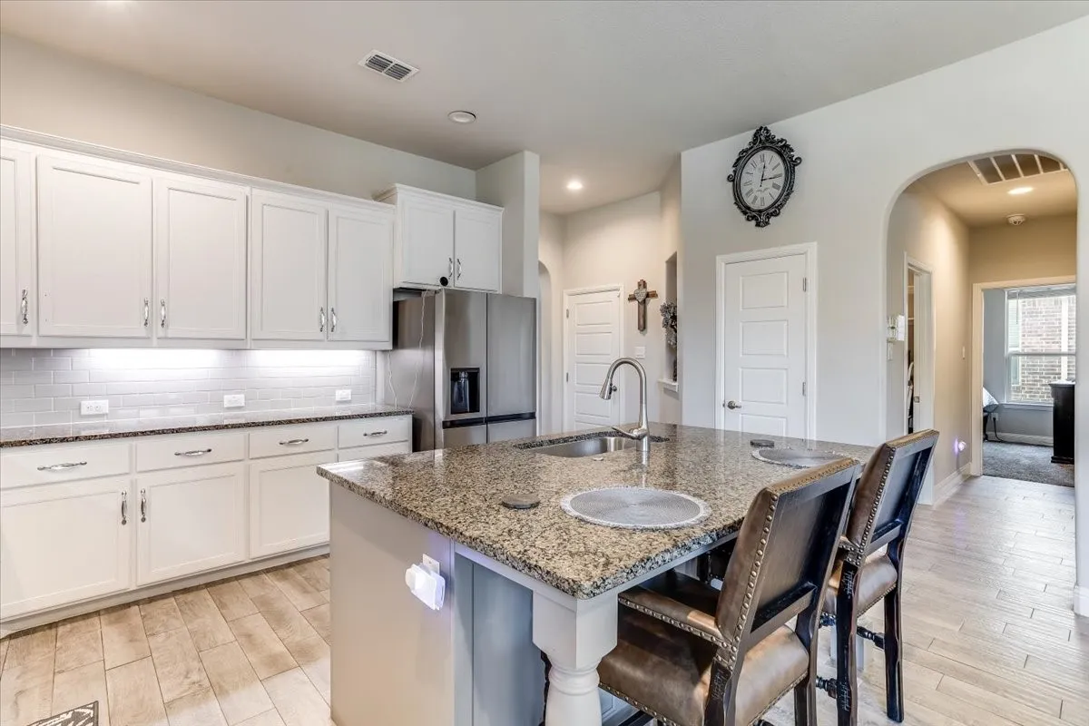 Kitchen featuring white cabinetry, subway tile backsplash, stainless steel appliances, a center island with a built-in sink, and wood-finish tile flooring