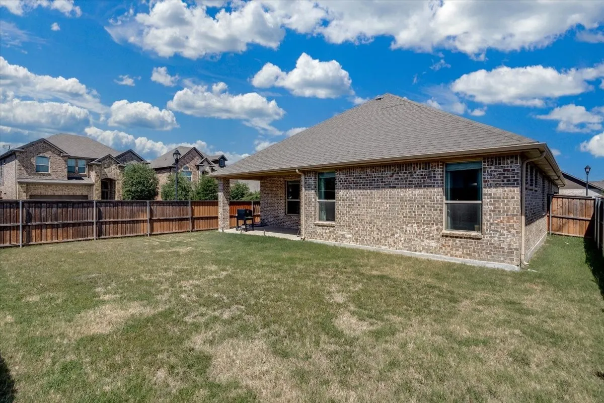 Expansive backyard featuring a natural grass lawn, full privacy fencing, and a covered patio area