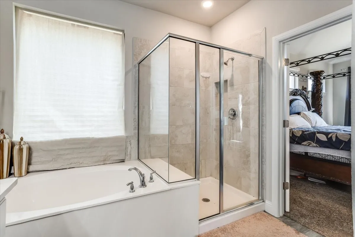 Built-in soaking tub with deck-mounted faucet, glass-enclosed shower with tile surround, and recessed lighting