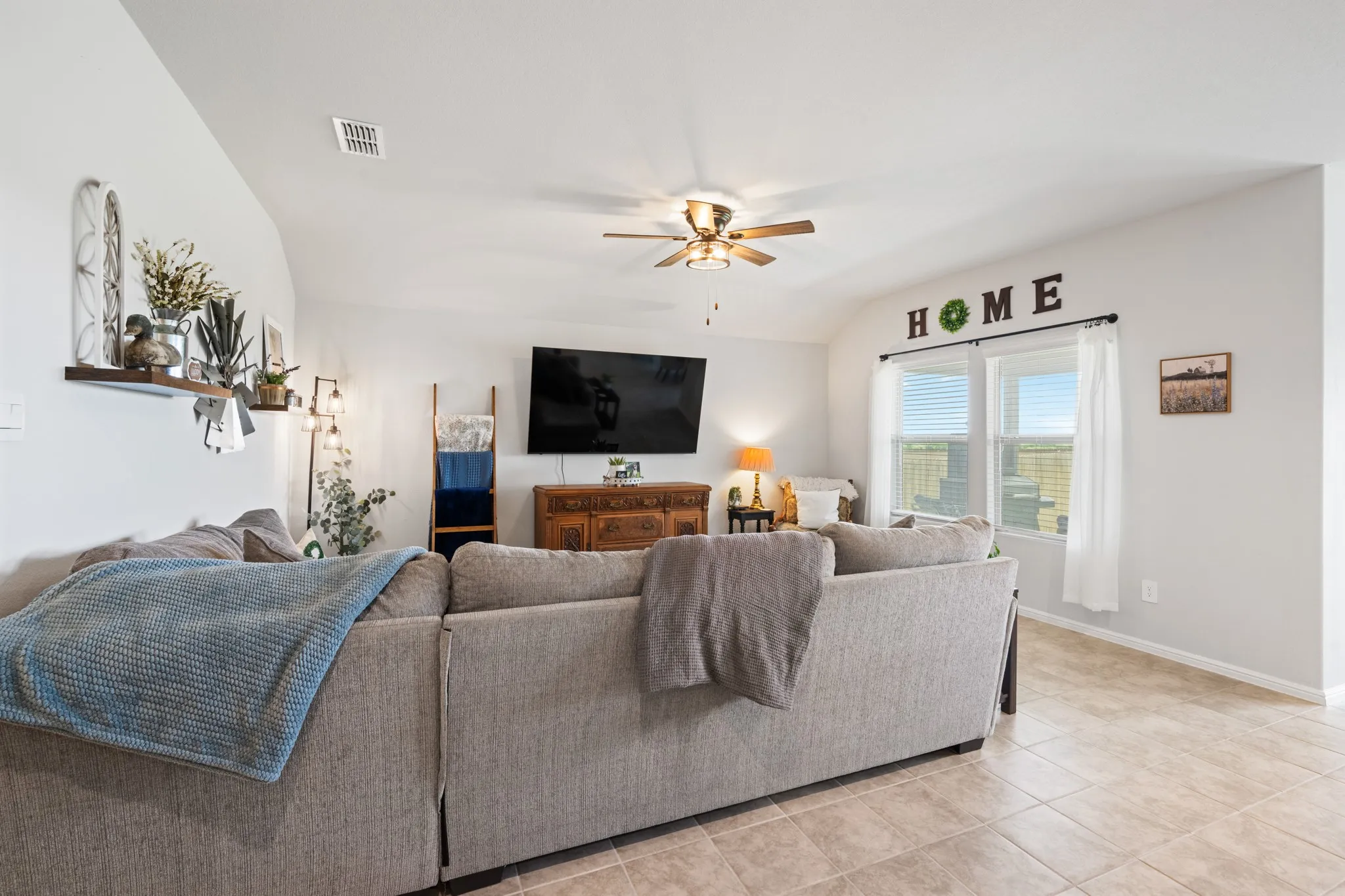Living room featuring ceiling fan, lofted ceiling, and light tile patterned flooring