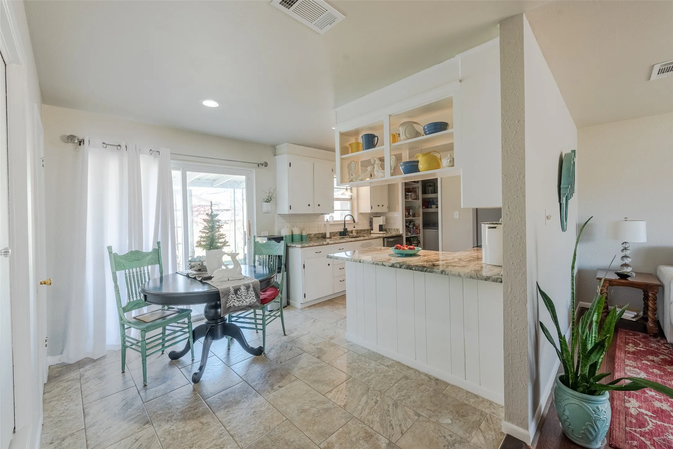 Kitchen featuring decorative backsplash, kitchen peninsula, light stone counters, sink, and white cabinets