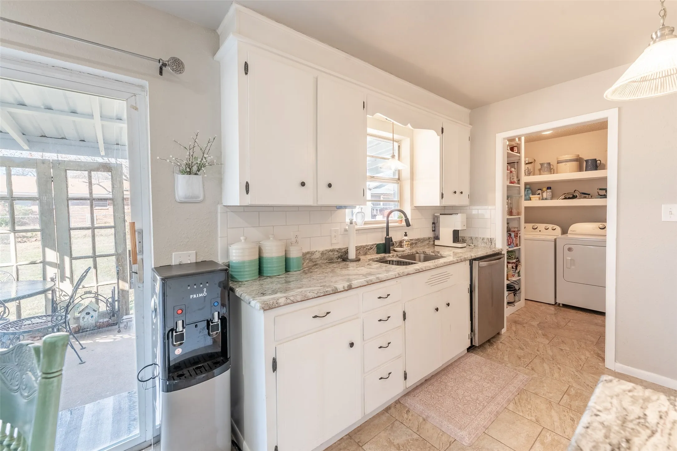 Kitchen featuring backsplash, sink, pendant lighting, washing machine and clothes dryer, and white cabinetry