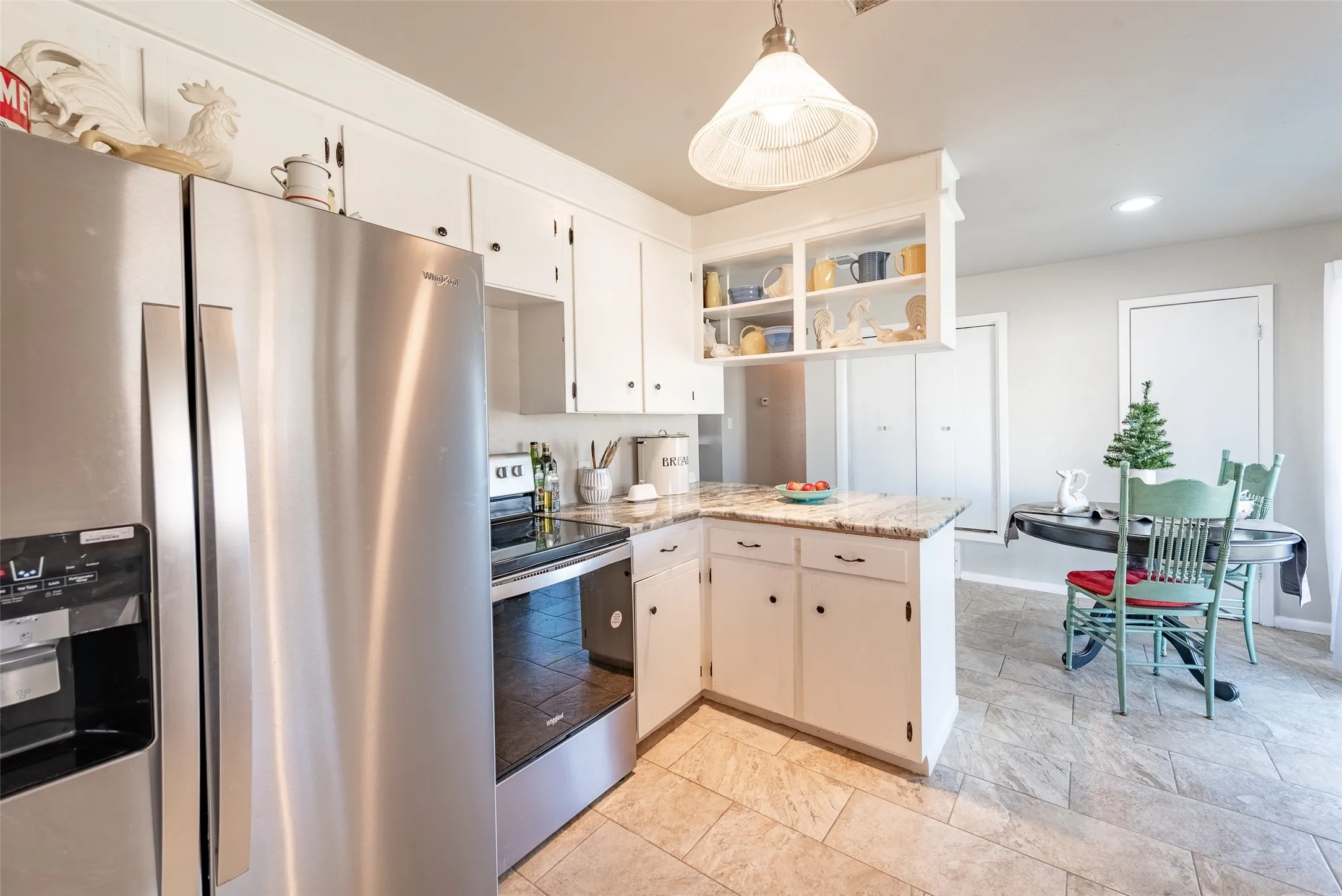 Kitchen featuring kitchen peninsula, light stone counters, stainless steel appliances, pendant lighting, and white cabinetry