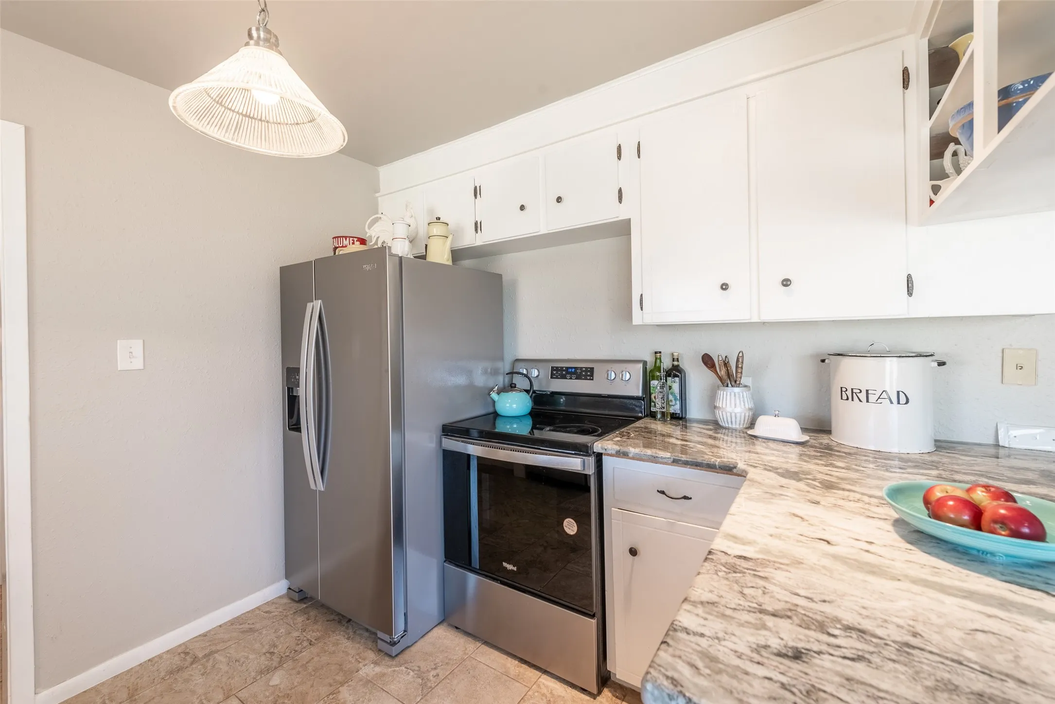 Kitchen featuring appliances with stainless steel finishes, decorative light fixtures, white cabinetry, and light stone counters
