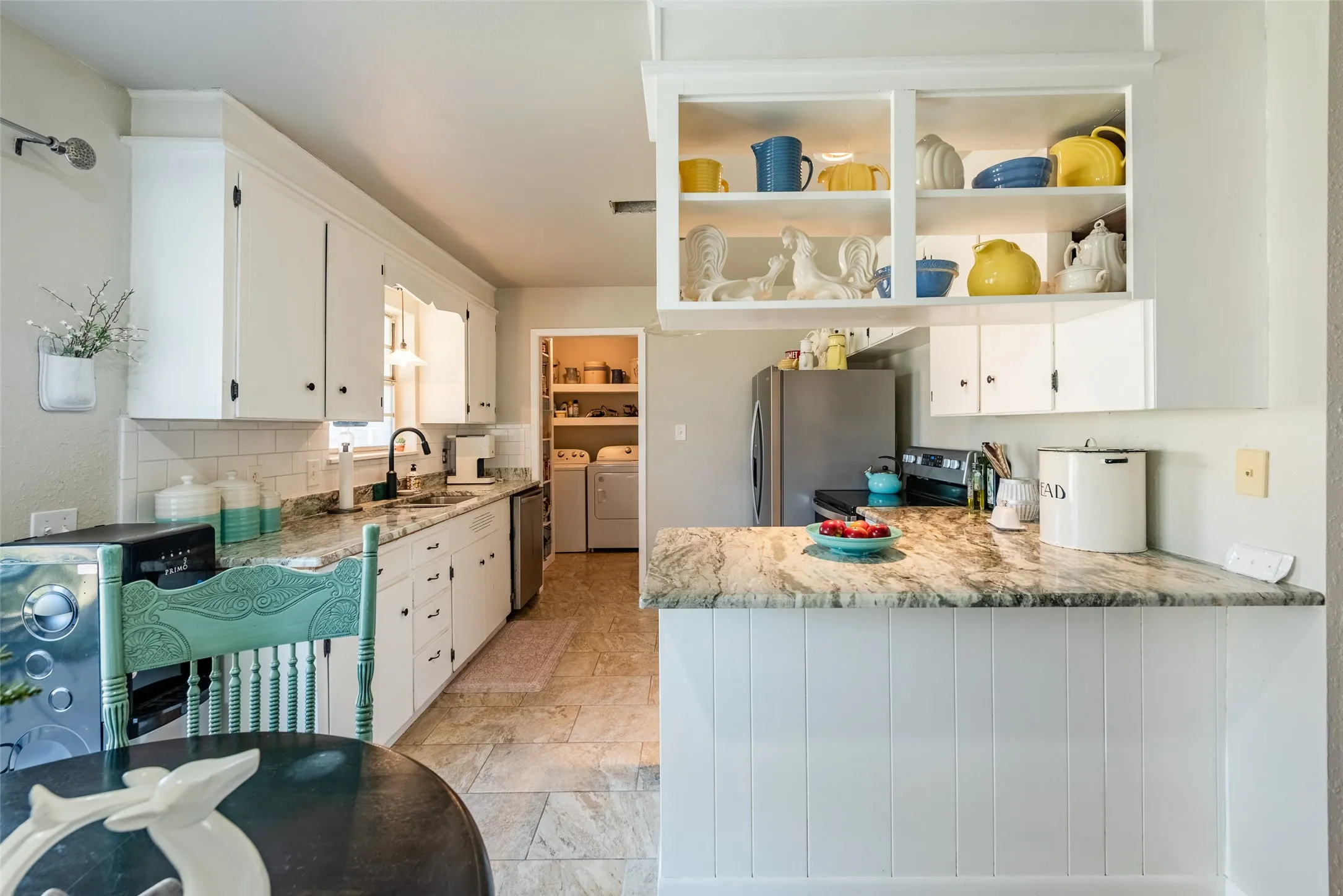 Kitchen featuring light stone countertops, stainless steel appliances, washer and clothes dryer, sink, and white cabinetry
