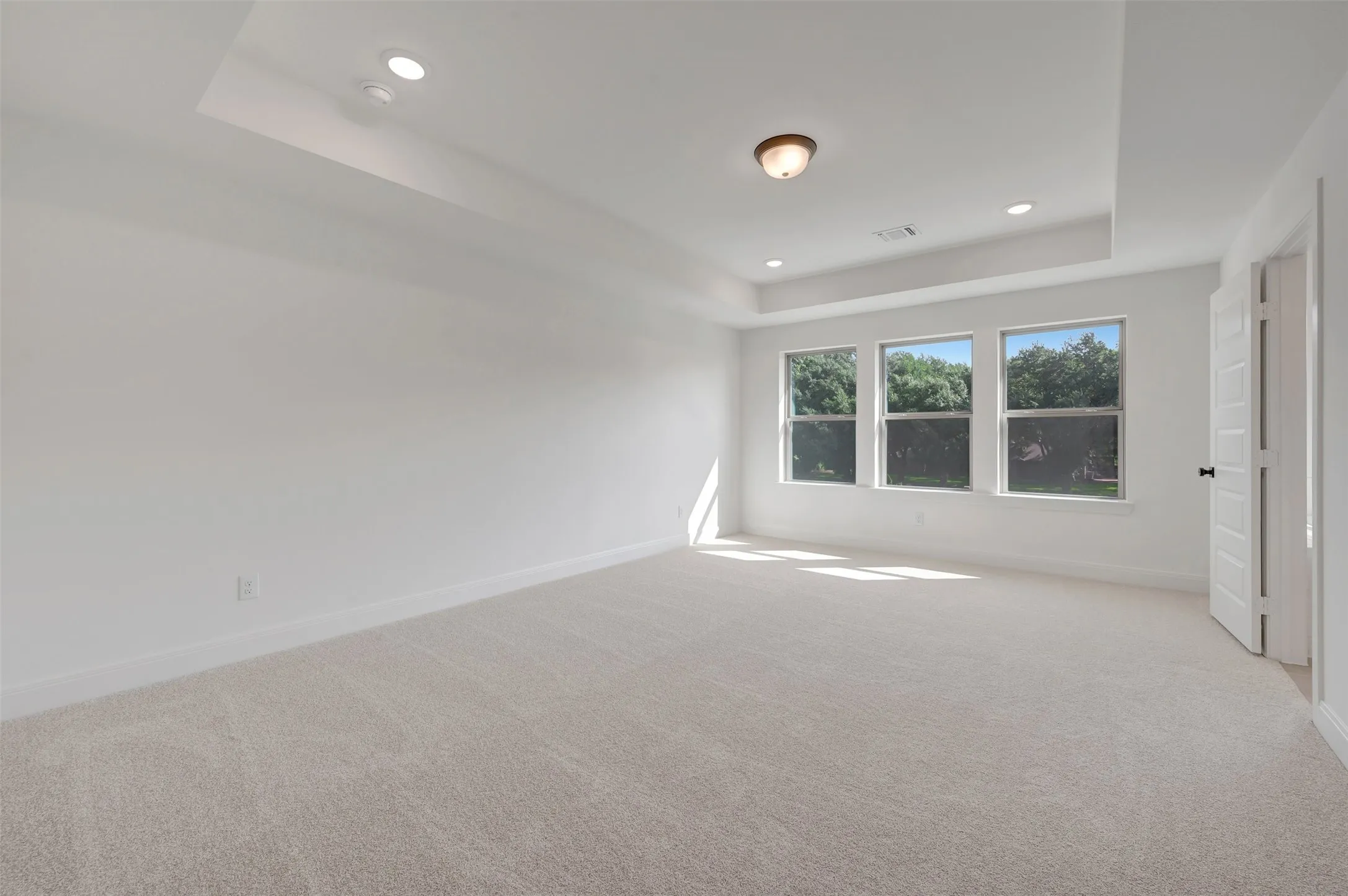 Spacious room with plush carpet flooring, a tray ceiling, and recessed lighting