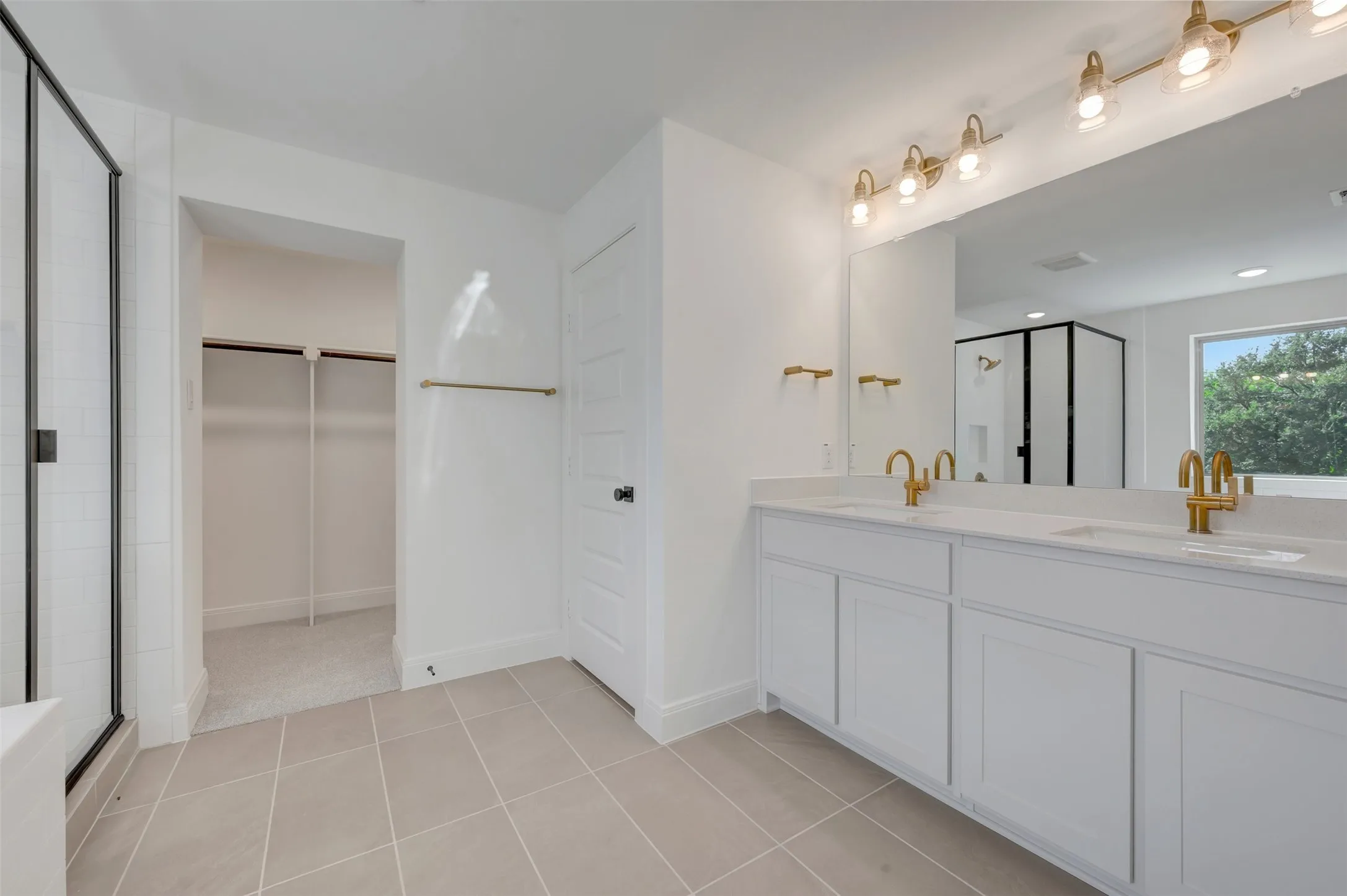 Bathroom featuring a double vanity with white cabinetry, light-toned countertops, and dual gold-finish faucets