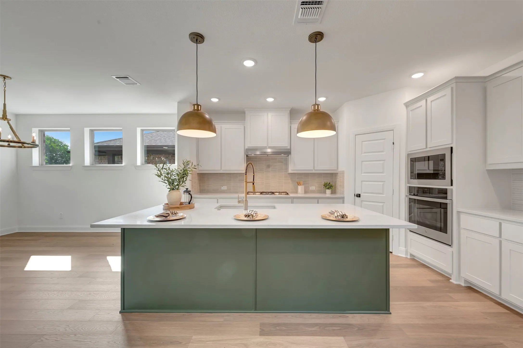 Open-concept kitchen featuring an expansive center island with a light countertop, white cabinetry, integrated stainless steel appliances, and wood-finish flooring