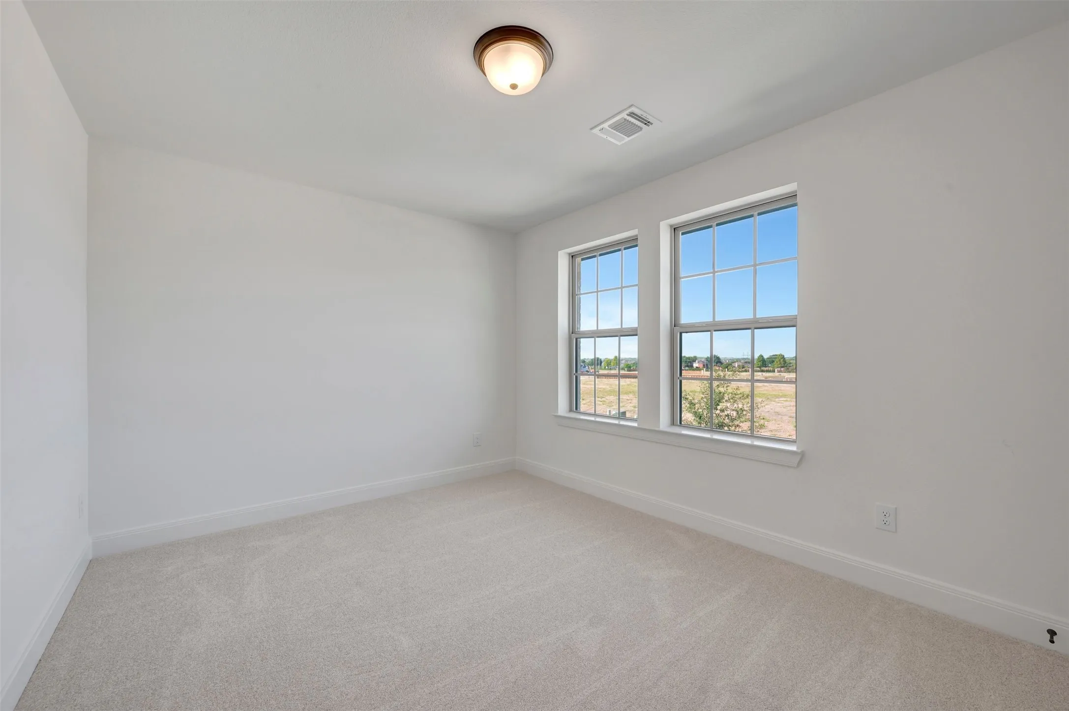Bright secondary bedroom featuring expansive double windows with grid-pane detailing, neutral carpet flooring, and soft overhead lighting