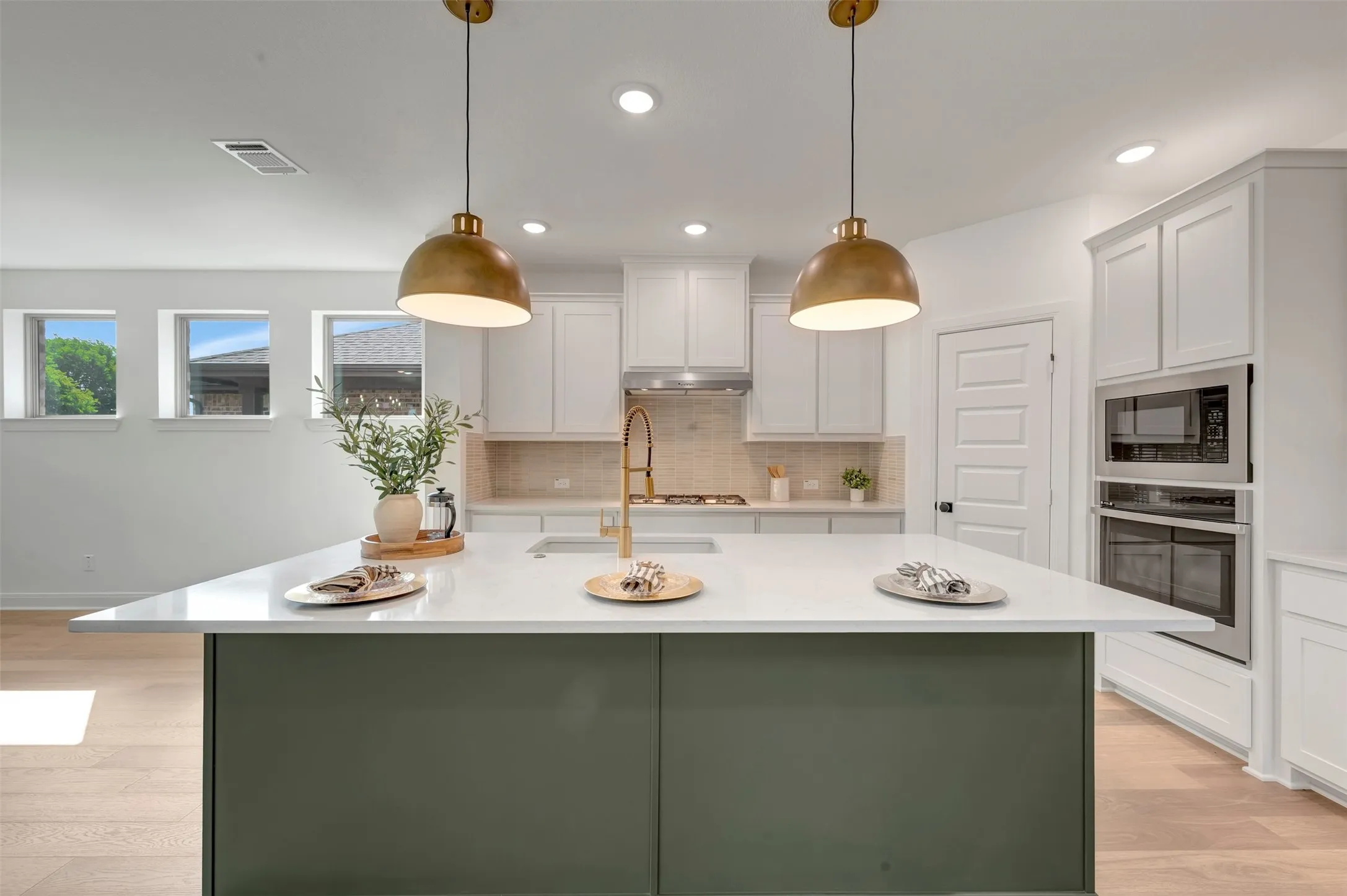 Kitchen featuring a large island with a light-toned countertop, white cabinetry, integrated stainless steel appliances, a tile backsplash, and wood-finish flooring