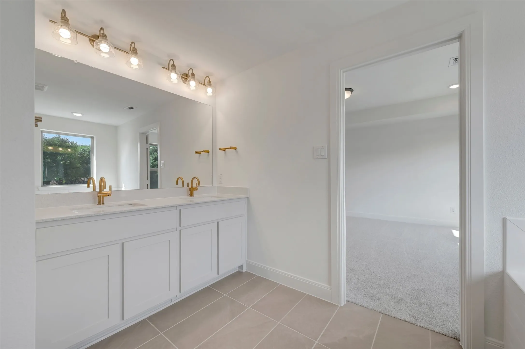 Bathroom featuring a dual vanity with white cabinetry, light-toned countertop, and gold-finish fixtures