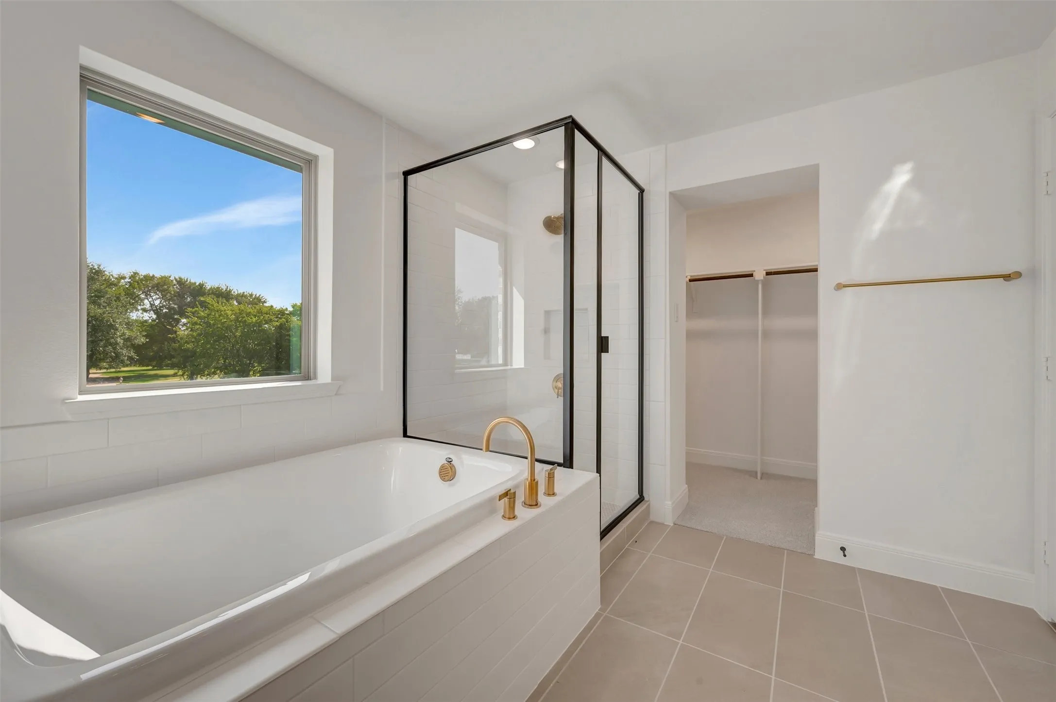 Modern bathroom featuring a built-in soaking tub with gold-tone fixtures, a glass-enclosed shower with black trim, and a separate walk-in closet
