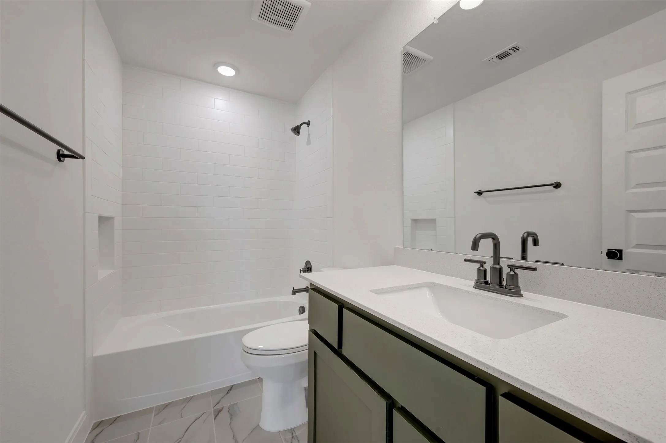 Bathroom featuring a white subway tile surround, built-in tub, and a vanity with a white countertop and rectangular undermount sink